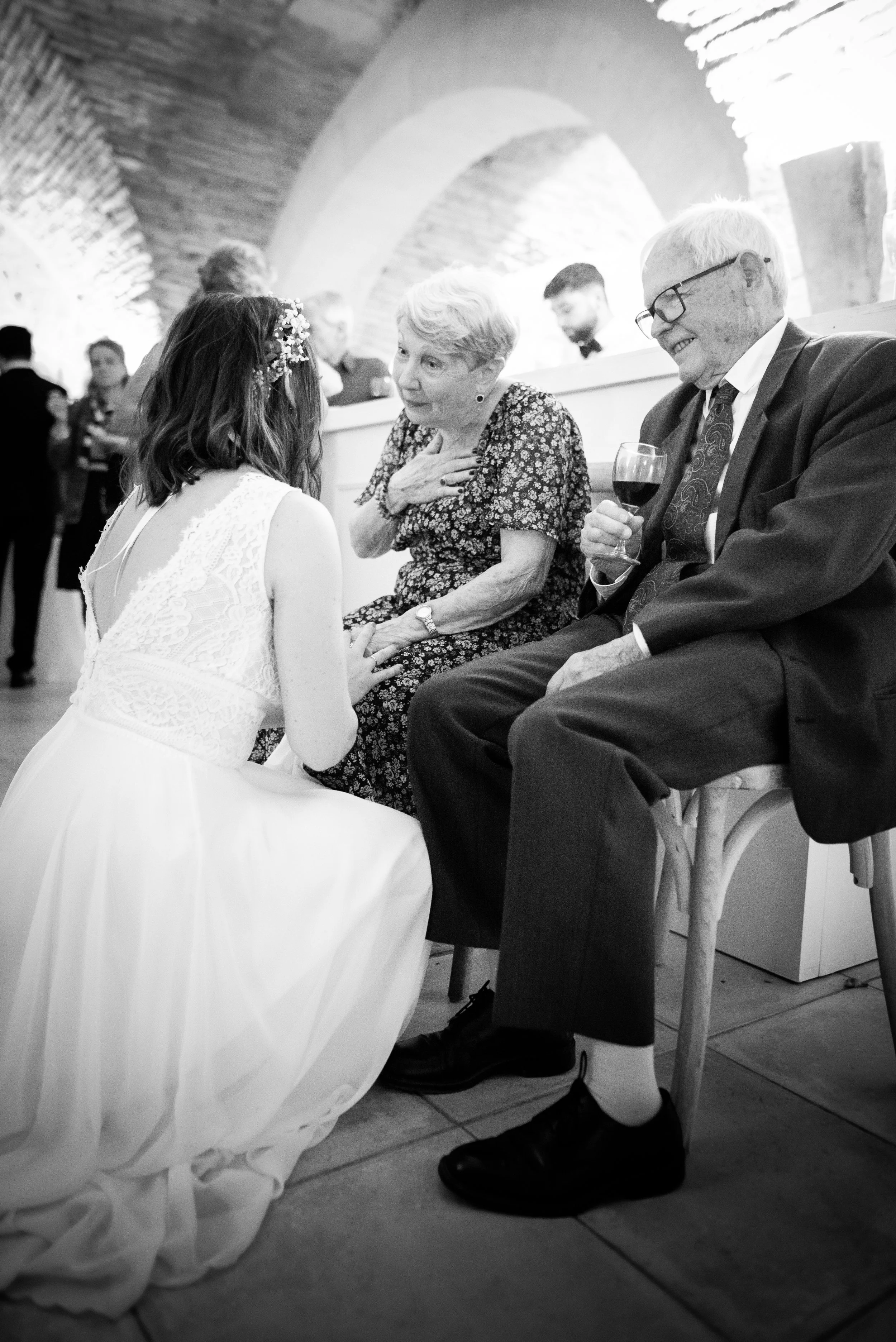 Une jeune femme en robe de mariage parlant avec une femme âgée et un homme âgé lors d'un mariage, tous assis et partageant un moment émouvant.