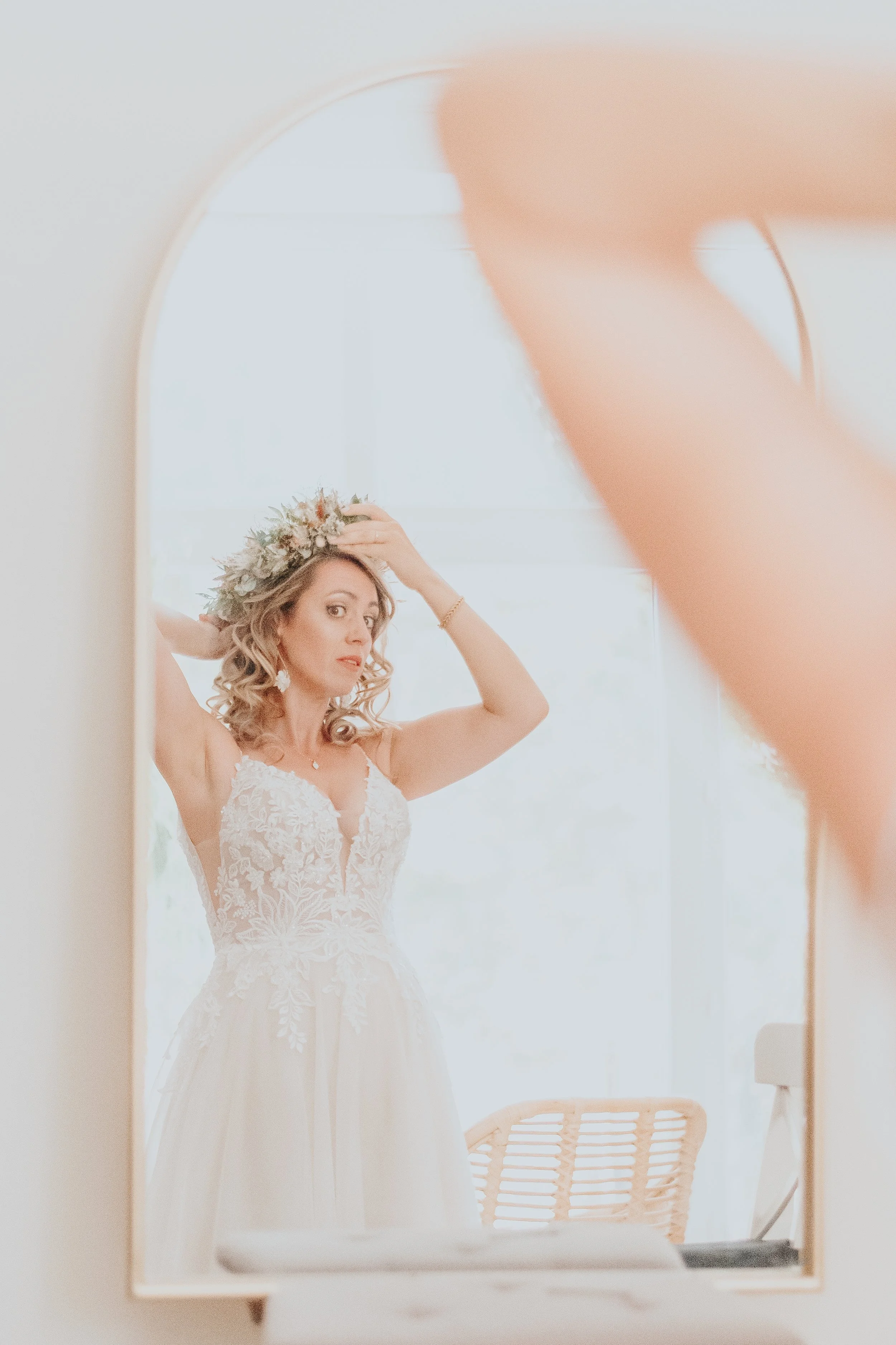Une femme en robe de mariée ajuste une couronne de fleurs sur sa tête devant un miroir