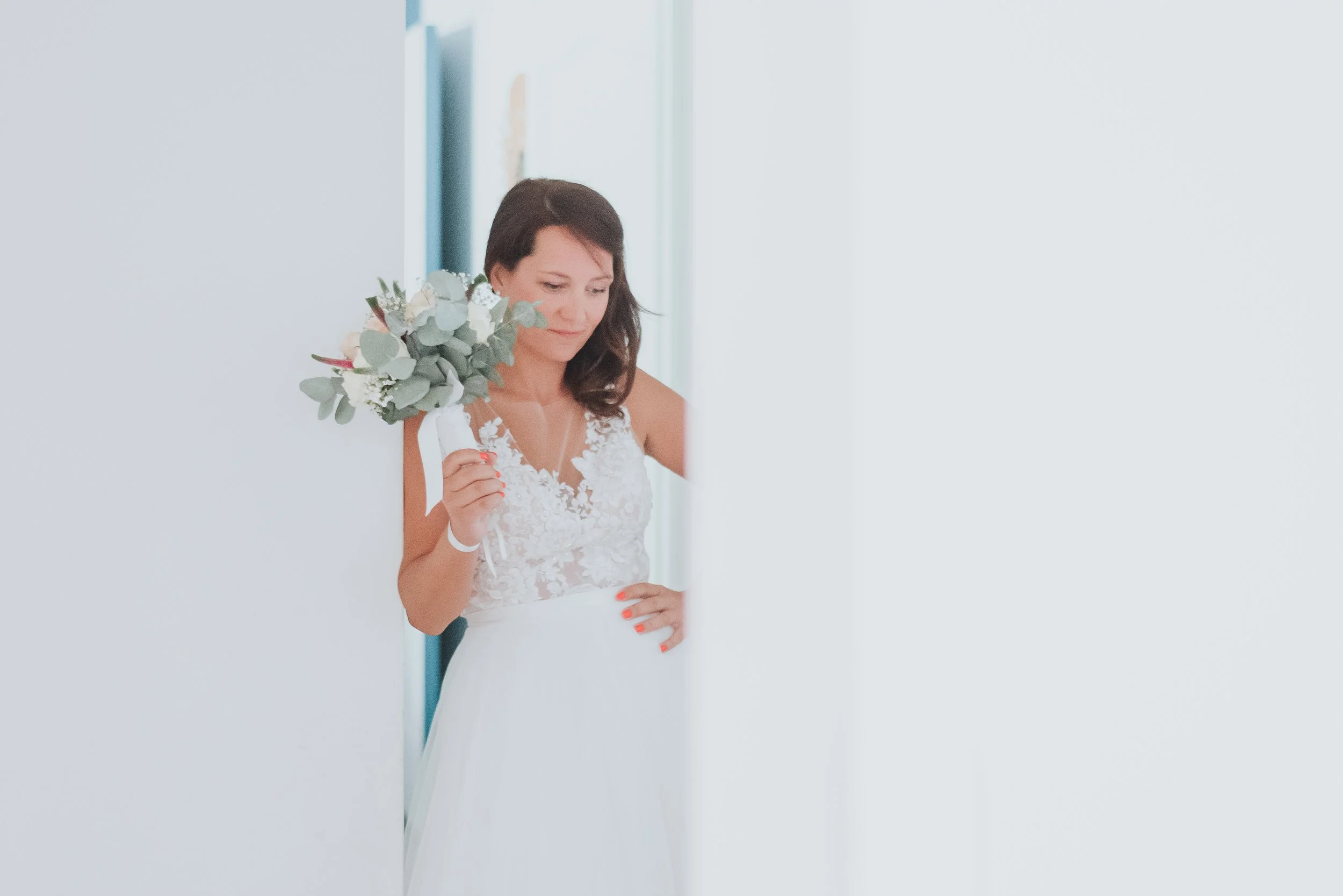 Femme en robe de mariage avec bouquet de fleurs, regardant à travers une porte entrouverte.
