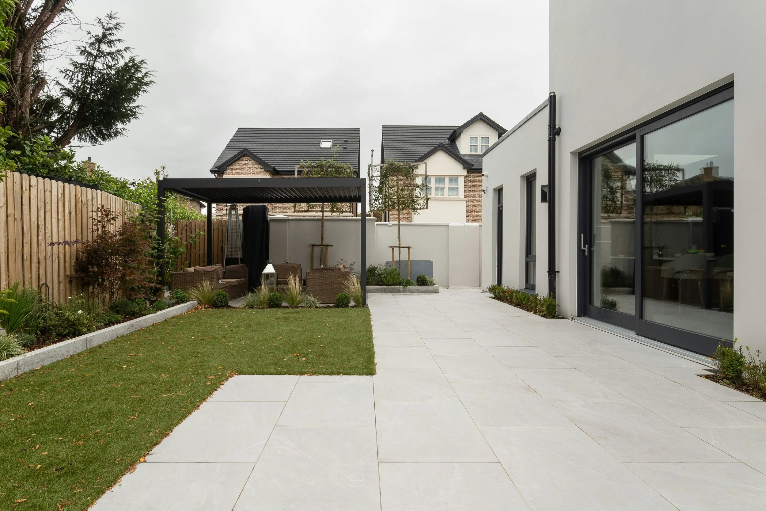 Modern backyard with a patio, sliding glass doors, small grassy area, garden bed, and a covered seating area with outdoor furniture.