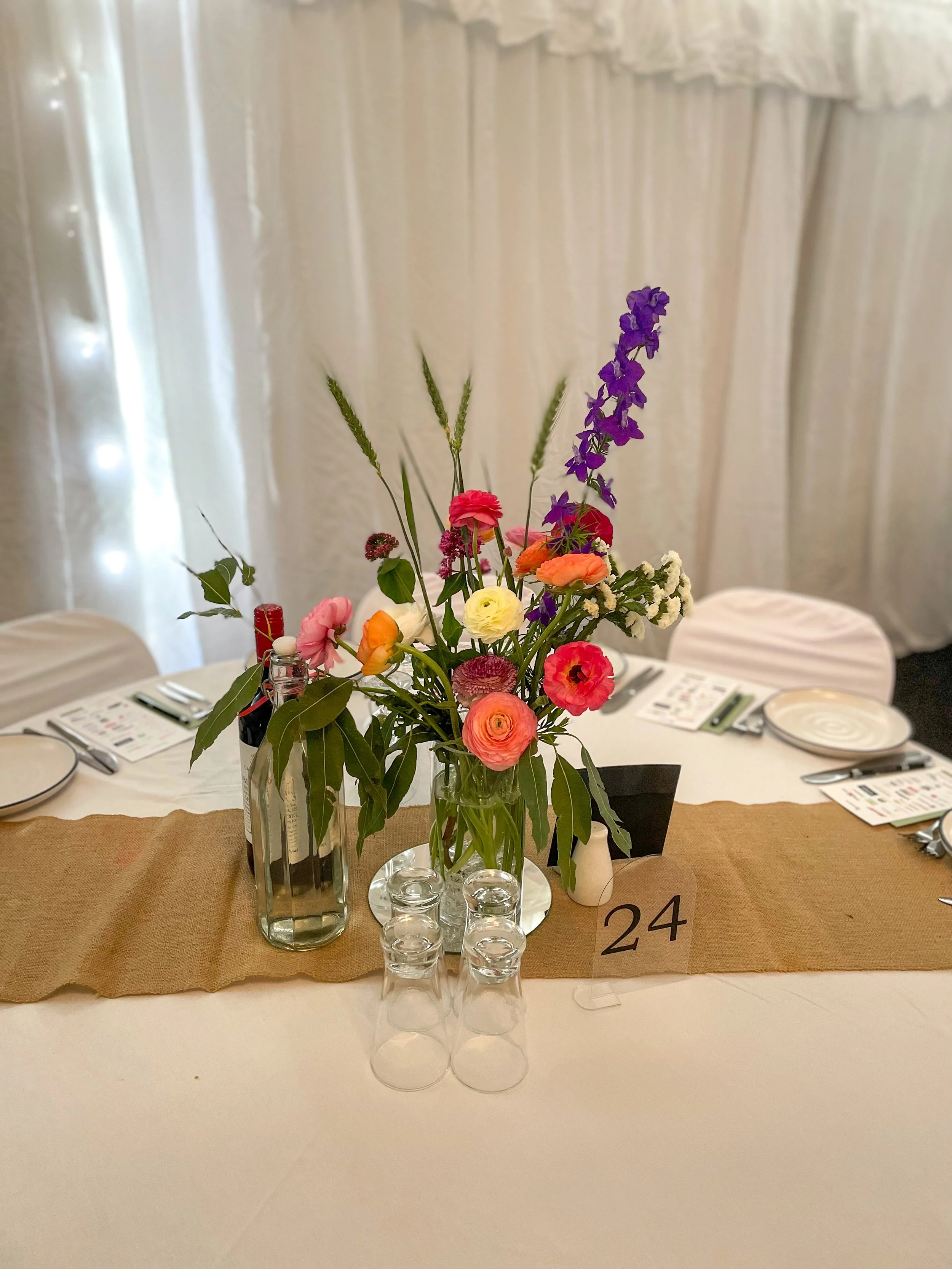 Table centerpiece with colorful flowers in three vases, table number 24, set for a formal event.