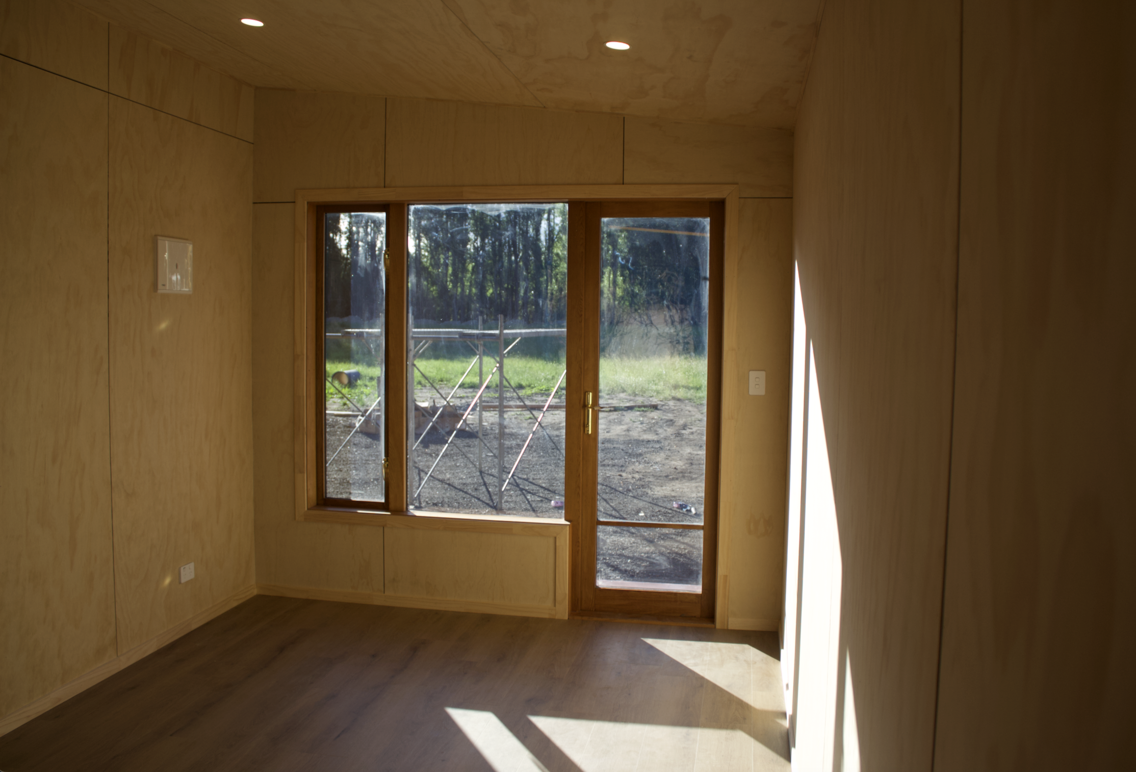 Interior of a room with wood-paneled walls and large glass double doors leading outside to a grassy area with trees.