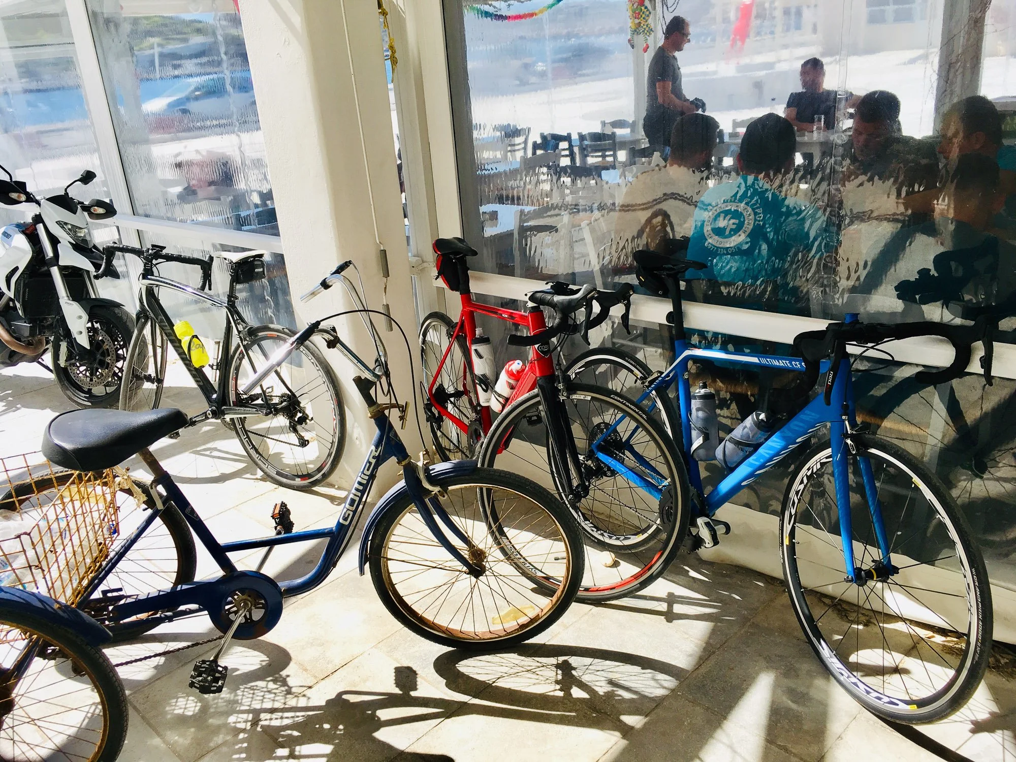 Several bicycles parked inside near a glass window, with people visible sitting in a restaurant or café behind the glass.