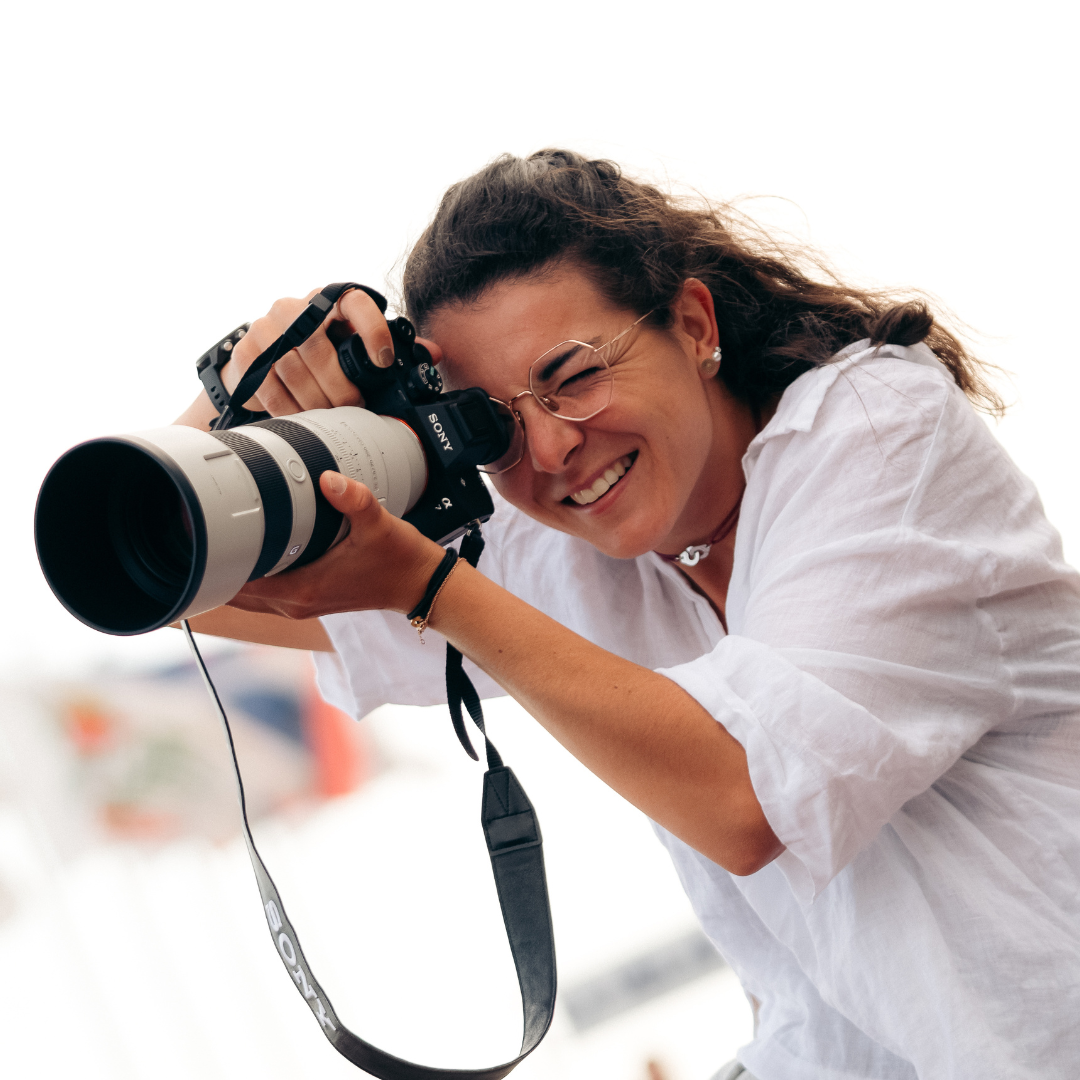 Une femme souriante tenant un appareil photo Sony avec un long objectif, en train de prendre une photo.