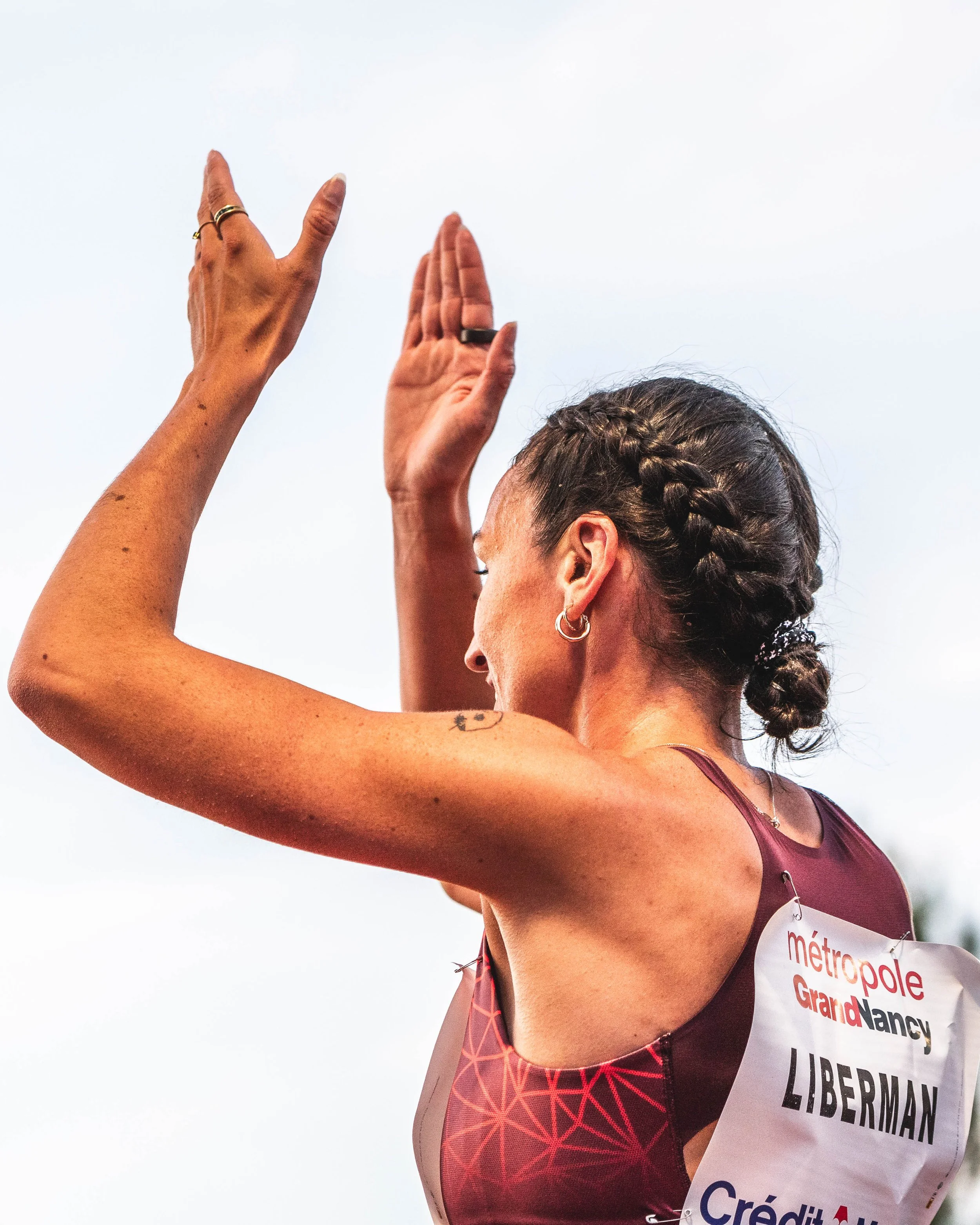 Une femme athlète lors d'une compétition, portant un dossard avec le nom LIBERMAN, levant les bras en signe de célébration ou d'encouragement.