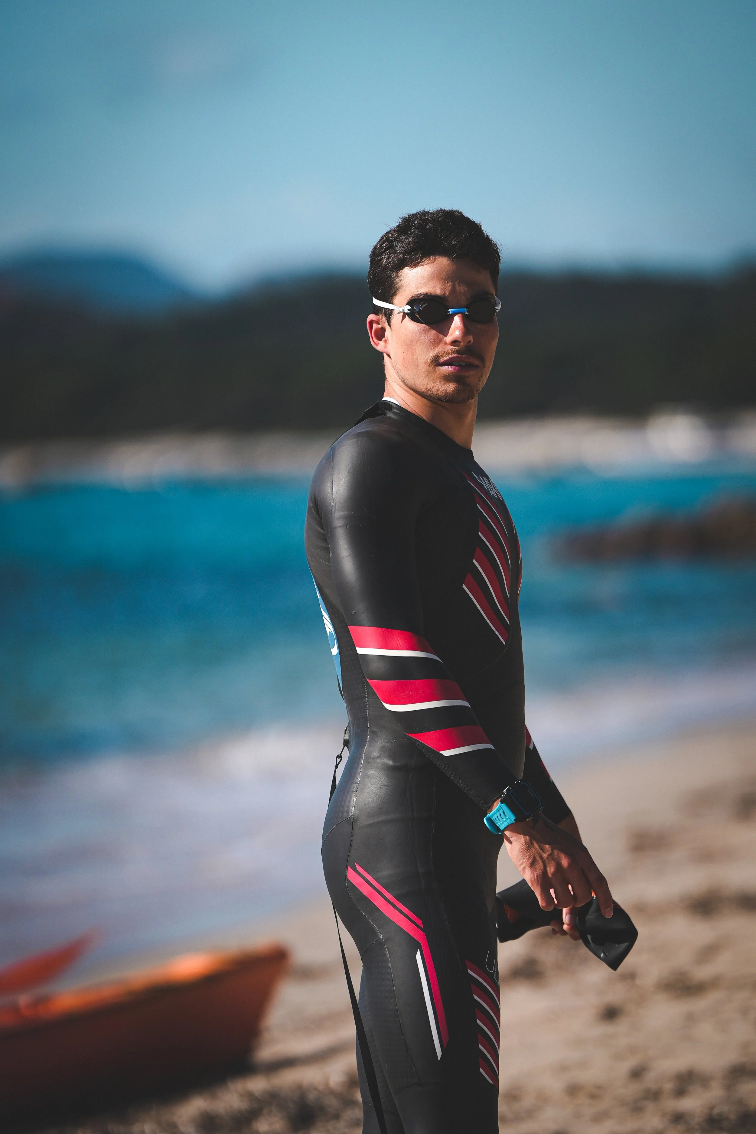 Valentin Morlec en combinaison de triathlon se tenant sur la plage avec la mer en arrière-plan.