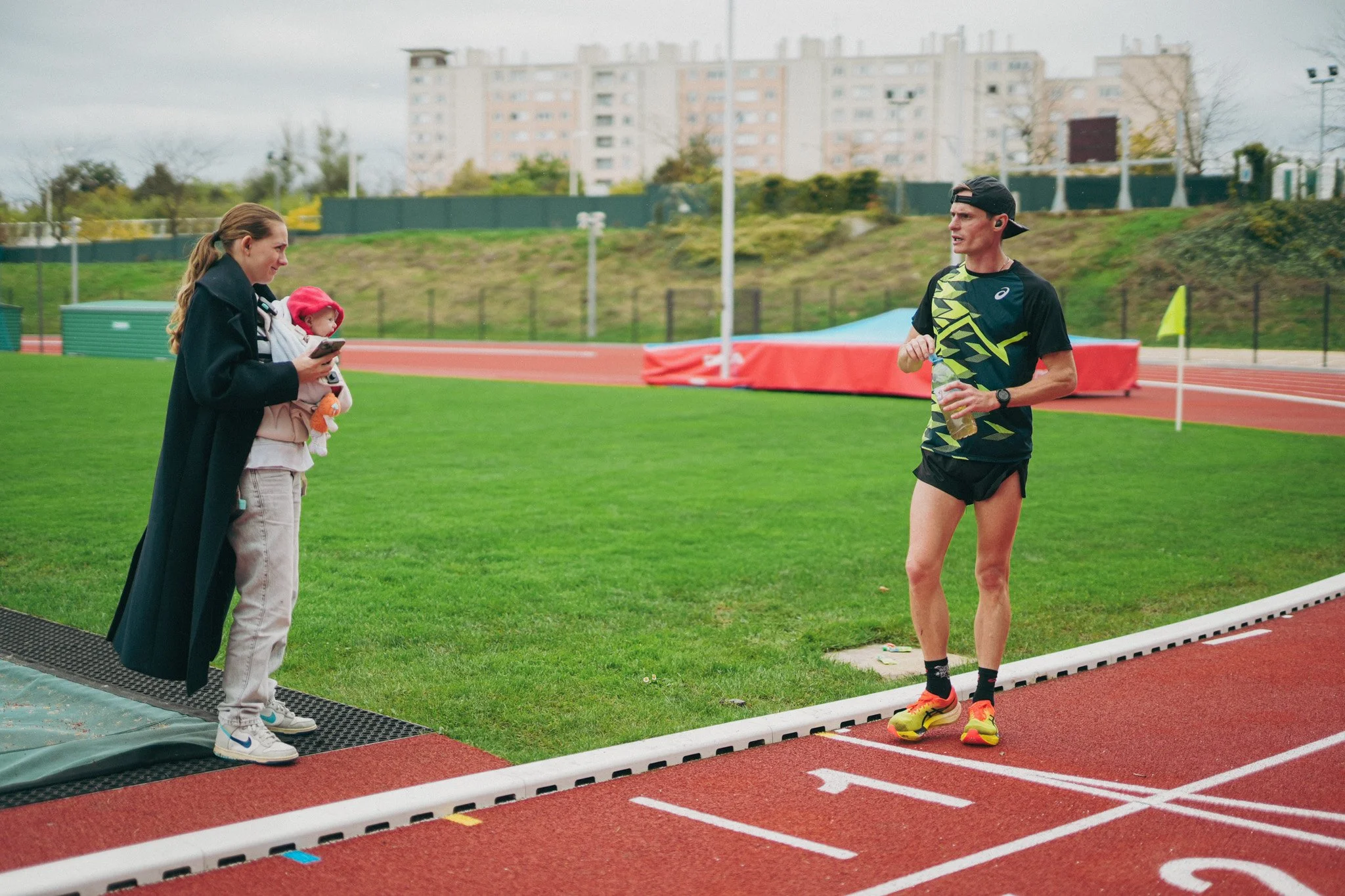 Aurélien Quinion en tenue de course discutant avec une mère et un enfant sur une piste d'athlétisme.