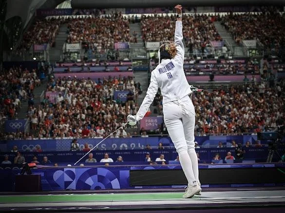Auriane Mallo-Breton célèbre sa victoire sur un podium dans un stade olympique, avec une foule nombreuse en arrière-plan.