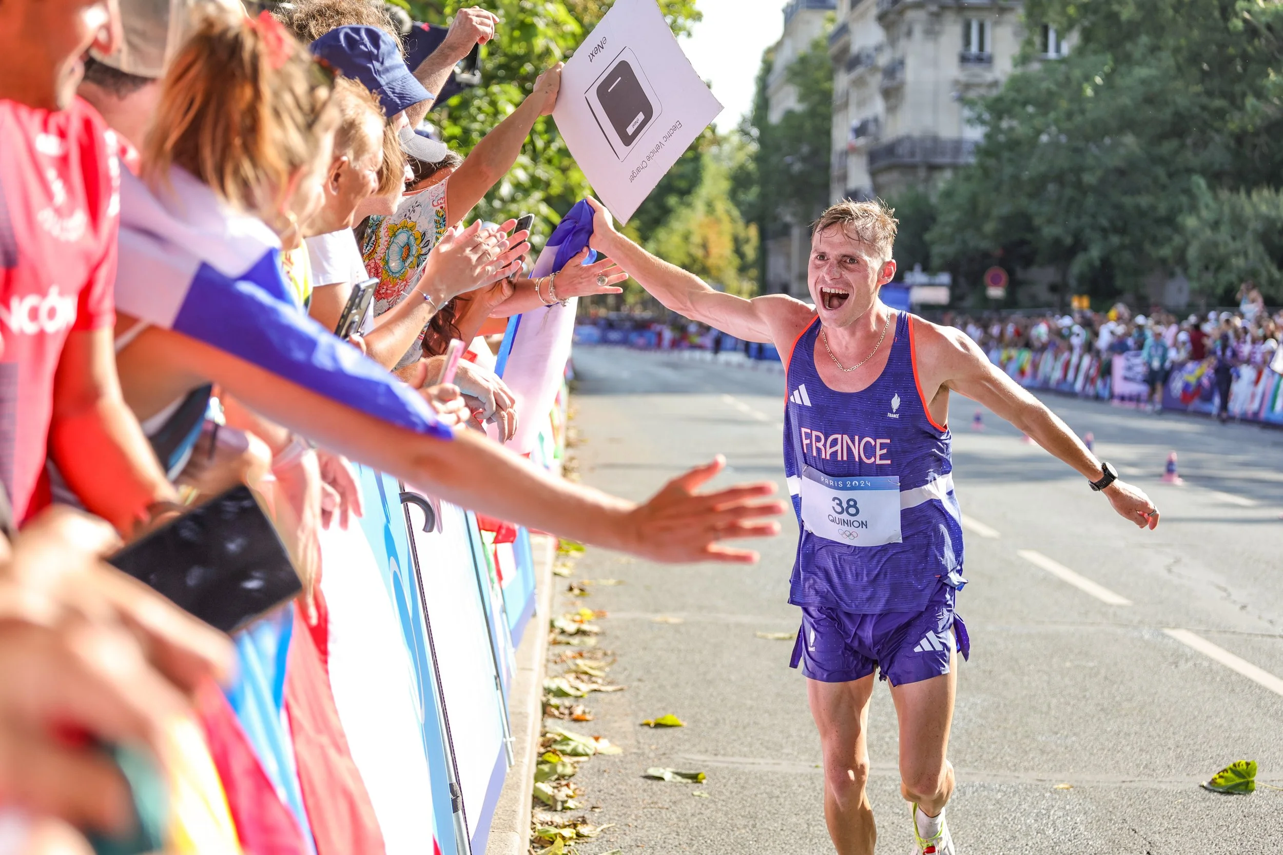Un coureur français souriant, vêtu d'une tenue bleue de course, félicité par des supporters lors d'une course en extérieur.