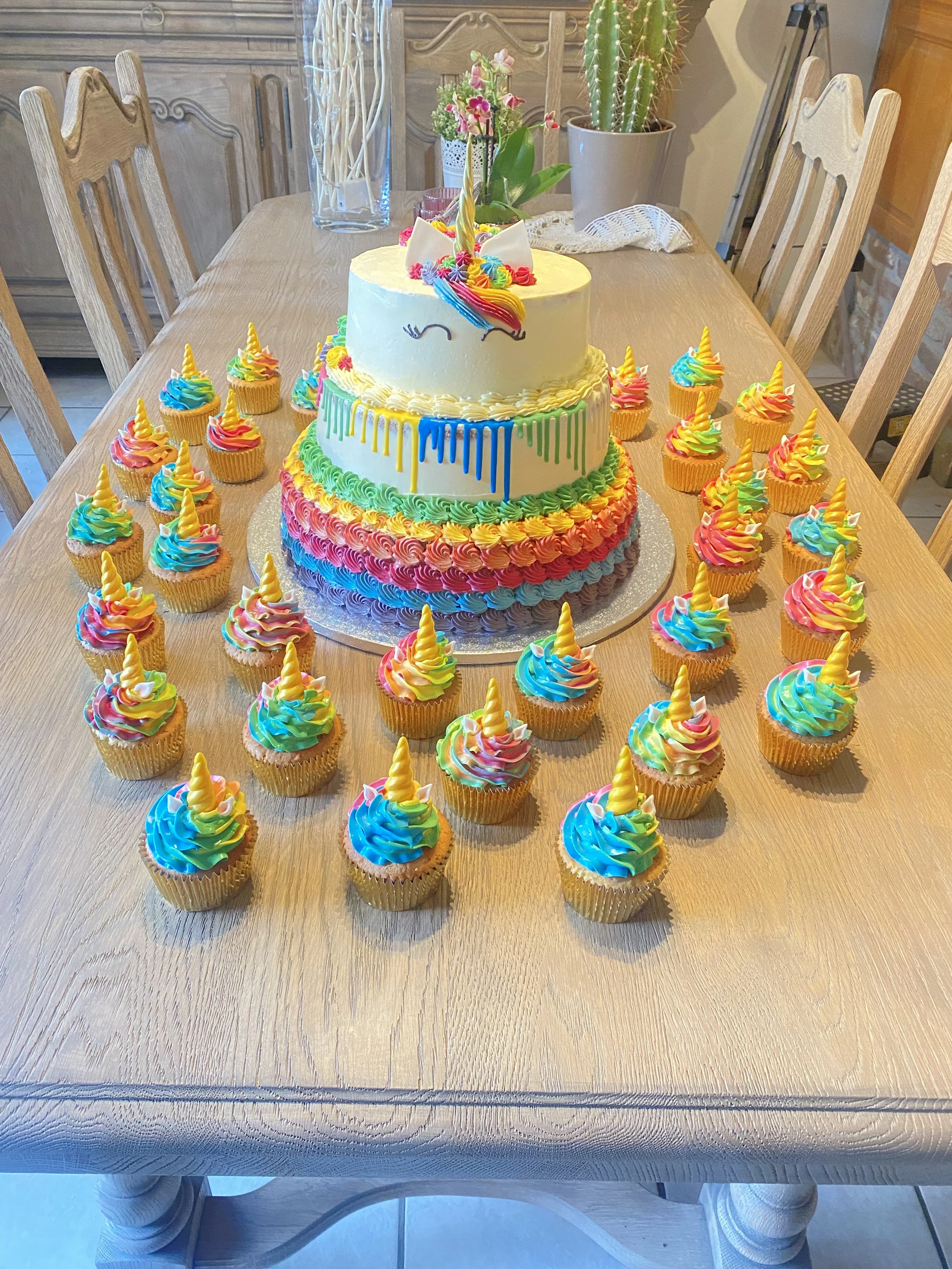 Een kleurrijk eenhoorn-taart met cupcakes eromheen, versierd met regenbooggeleidehoorns en kleurrijke glazuur.