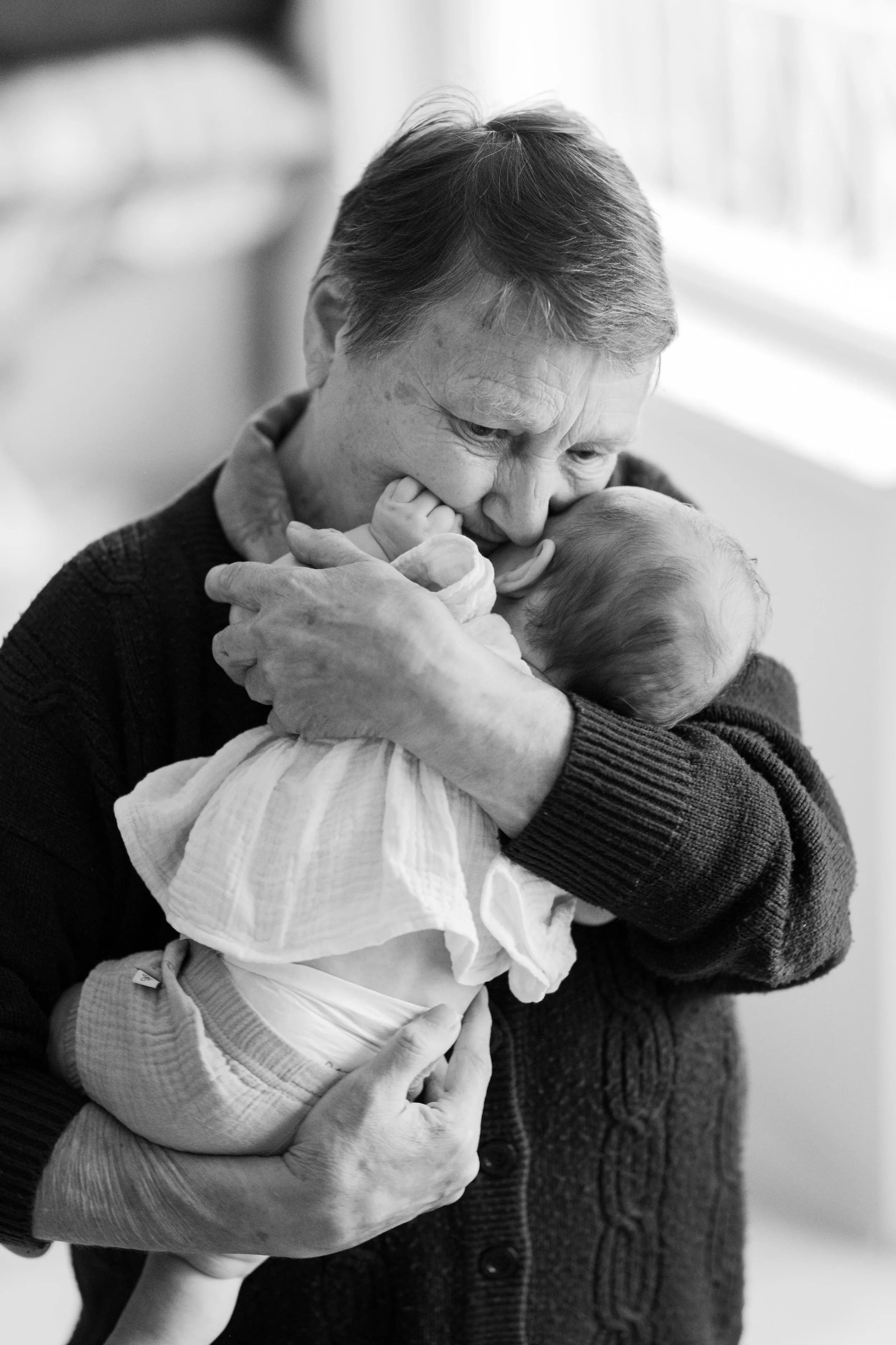 An elderly woman holding a baby close, embracing lovingly in a black and white photo.