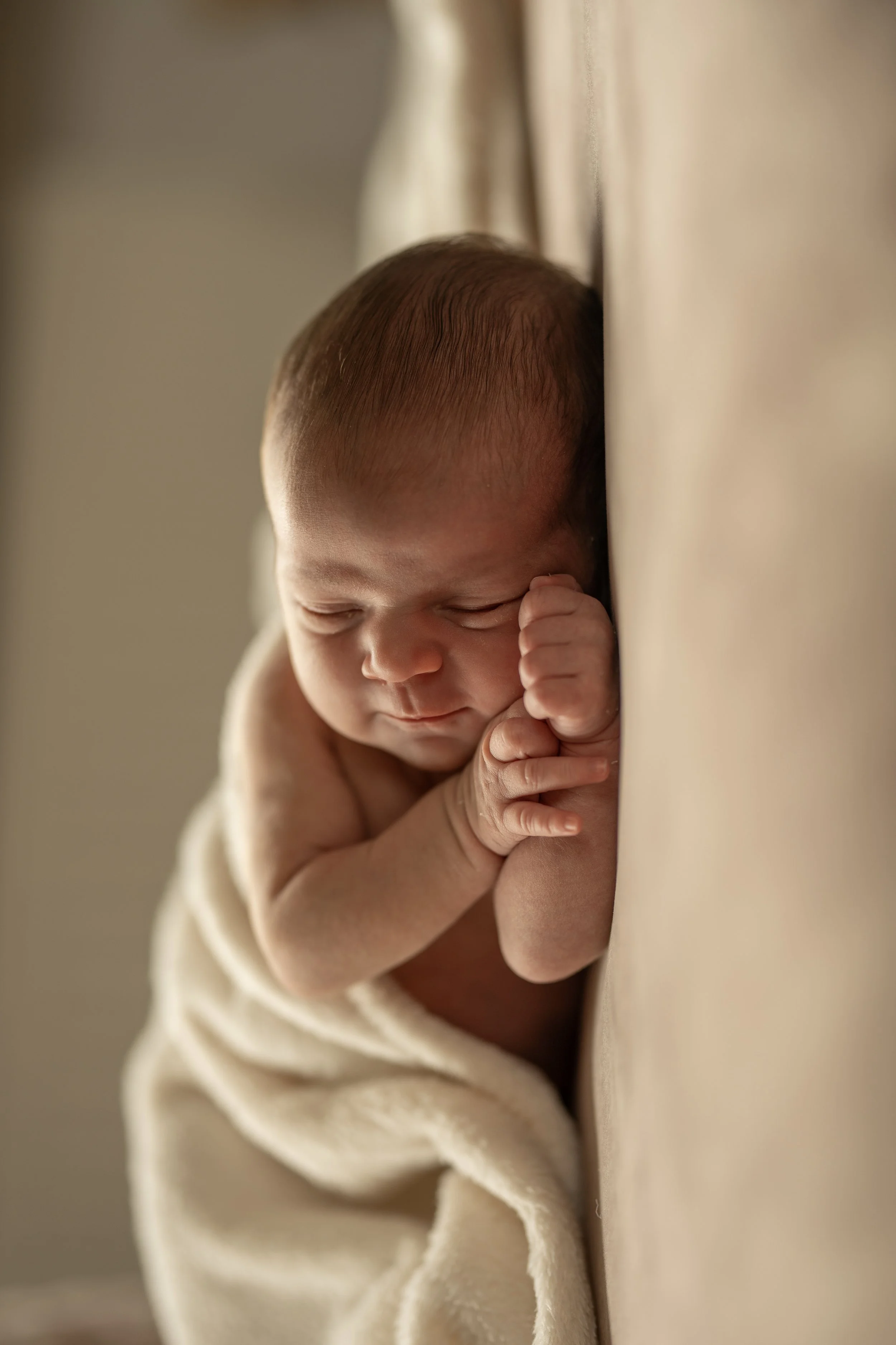 A newborn baby sleeping peacefully, pressed against a soft surface with a blanket wrapped around the lower body.