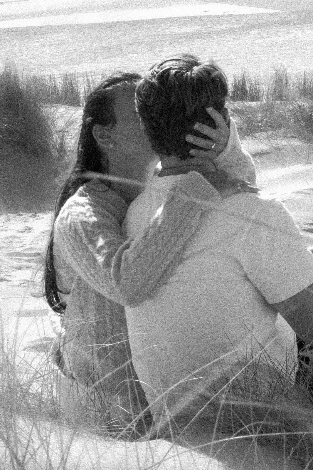 A couple sharing a kiss on the beach in black and white.