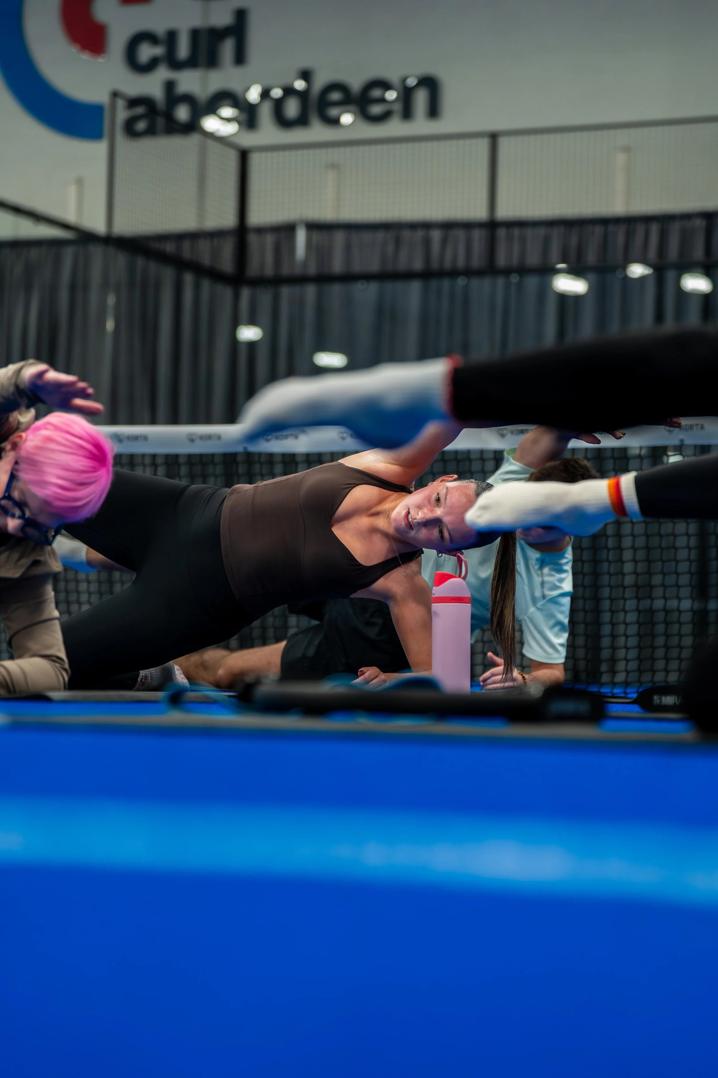 A group participating in pilates in an indoor sports facility with a net in the background.