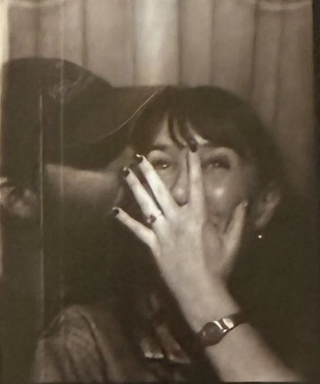 Two women sharing a laugh, one covering her mouth with her hand, in black and white.