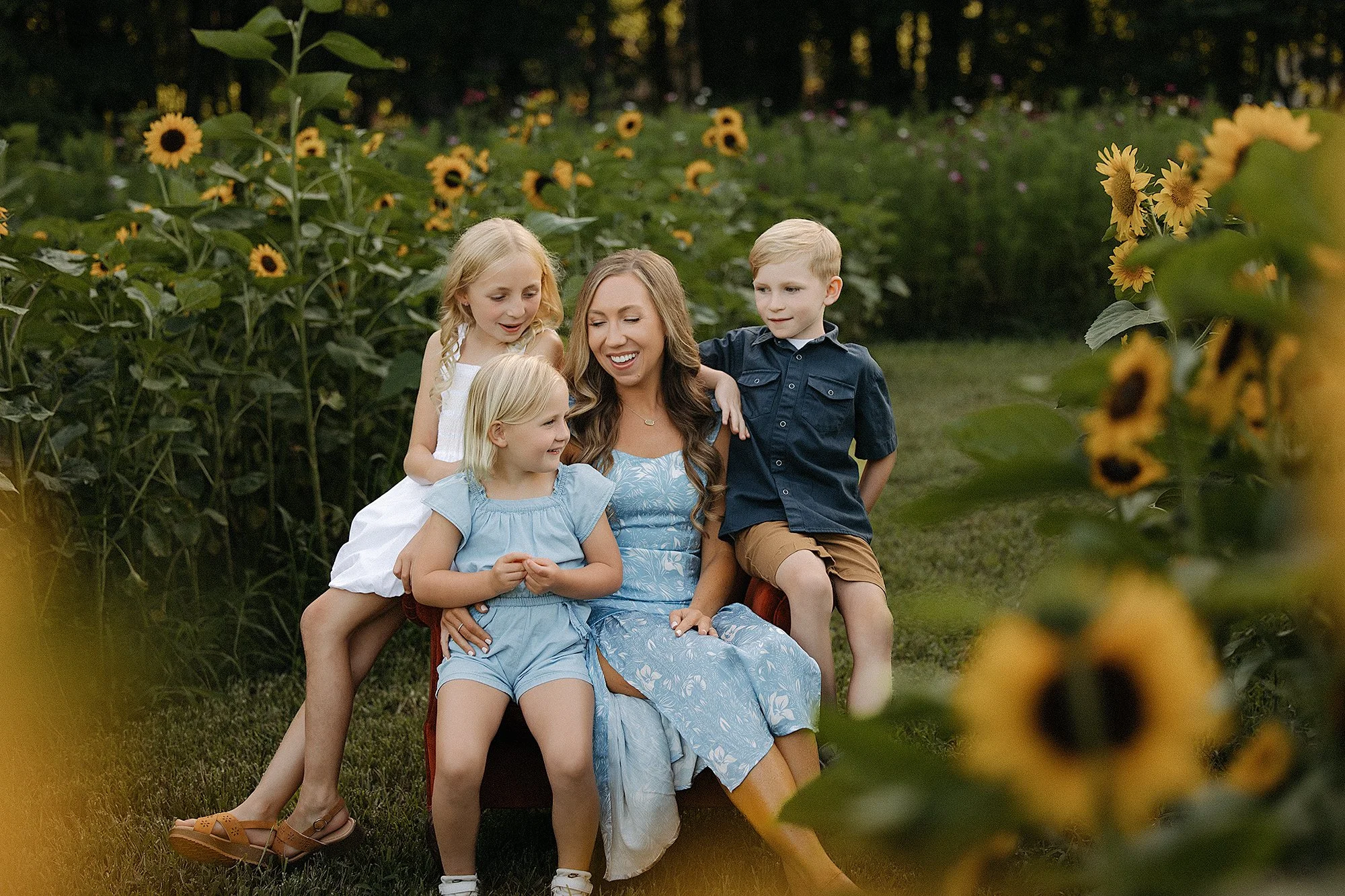 A mother and her children enjoy a sunny day in a field of blooming sunflowers, captured during a mini photo session