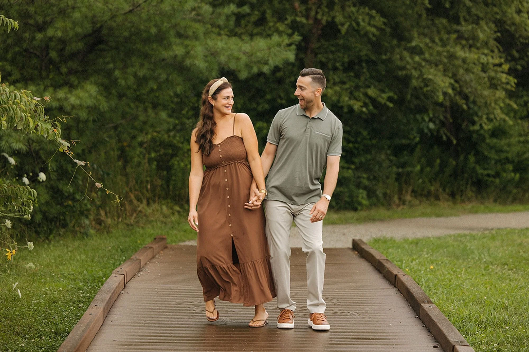 A couple walking hand in hand across a wooden bridge at MacGregor Park in Westfield, Indiana.