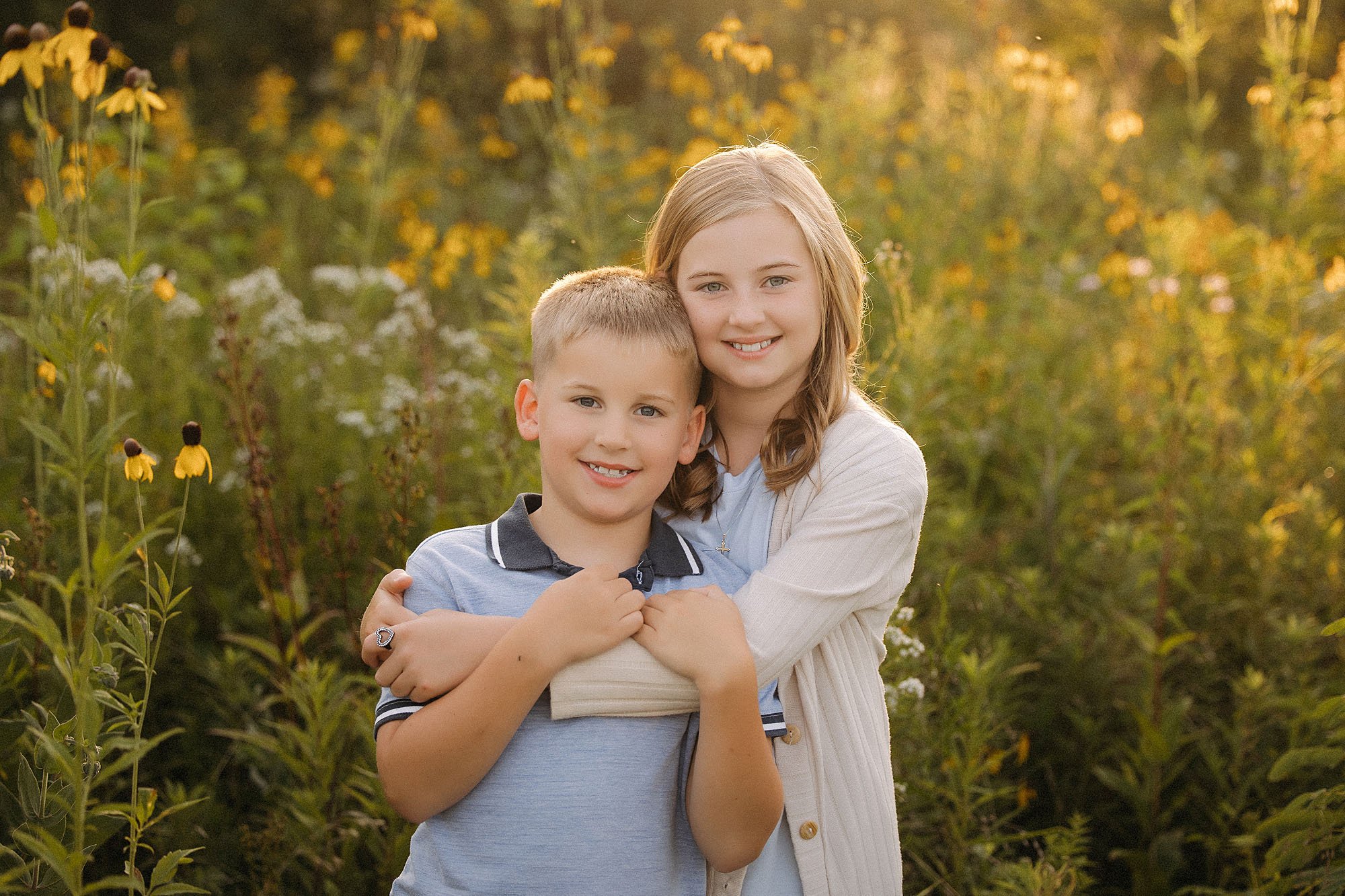 Brother and sister hugging and smiling together in wildflowers during a family maternity session in Westfield Indiana