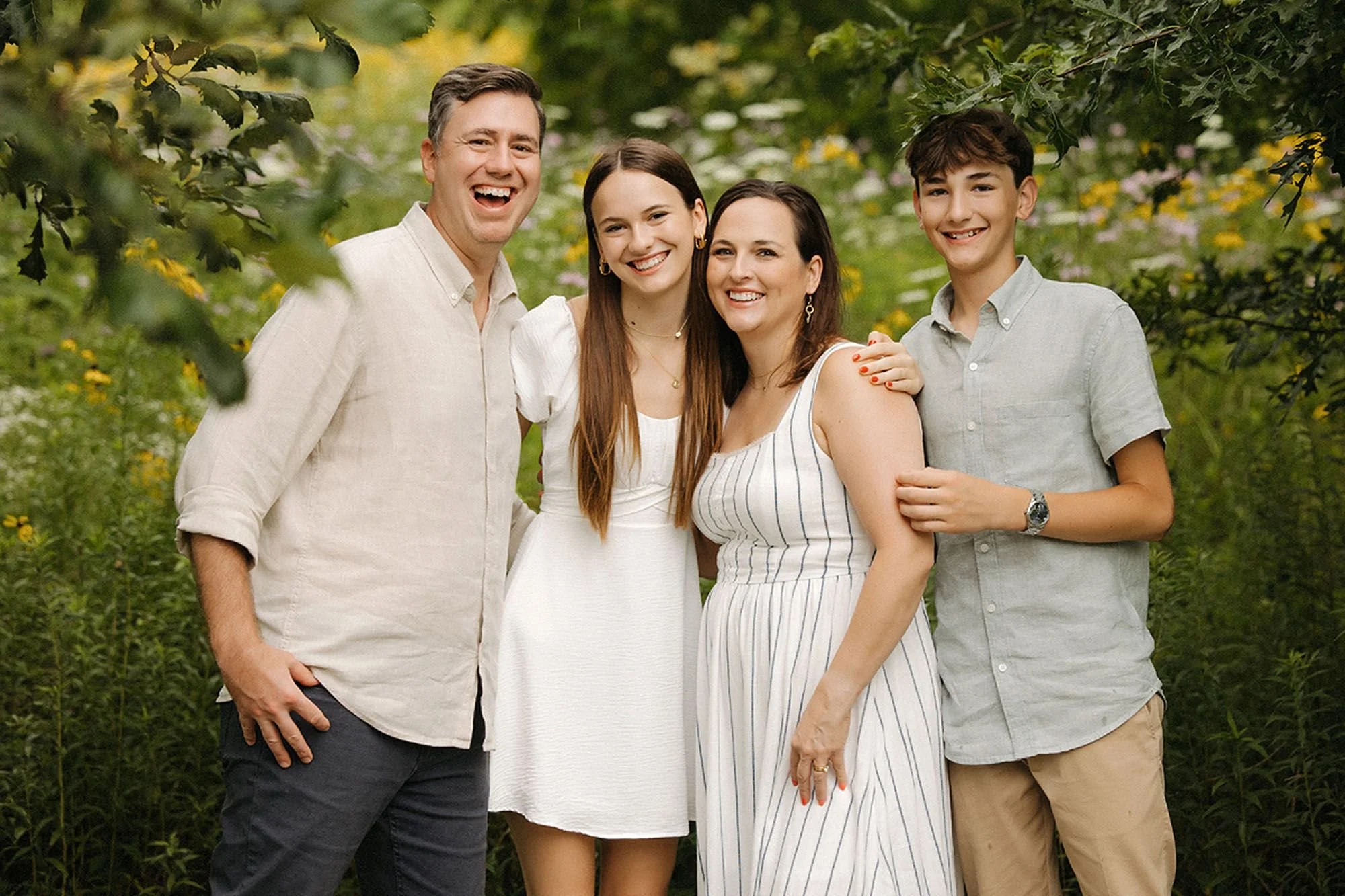 Parents and their two children smiling together while surrounded by wildflowers during a summer family session.