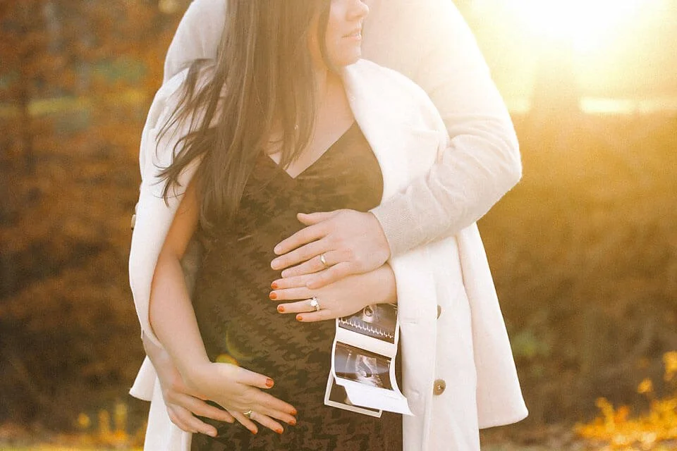 Pregnancy Announcement Photos featuring a couple lovingly celebrating their growing family while displaying ultrasound images during a warm autumn evening.