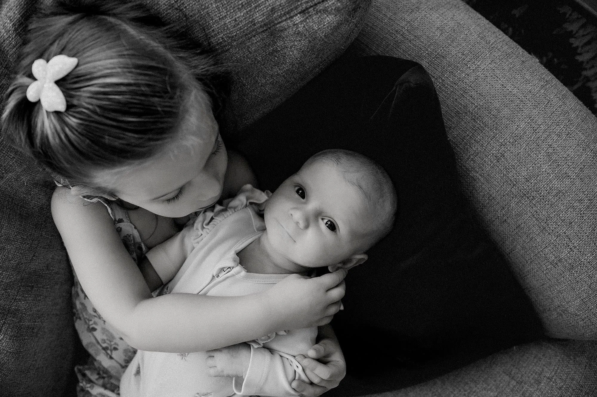 black and white image of sister holding infant sibling- what is newborn lifestyle photography