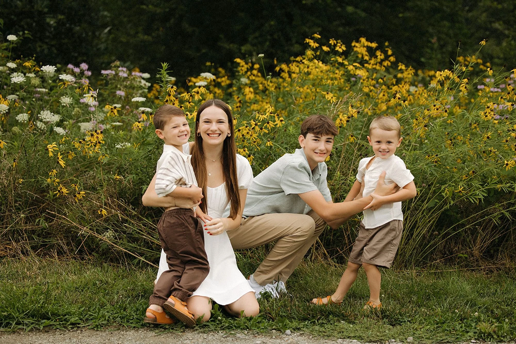 Teenage siblings playfully interacting with their younger brothers in a wildflower field during a summer extended family session in Westfield, Indiana.