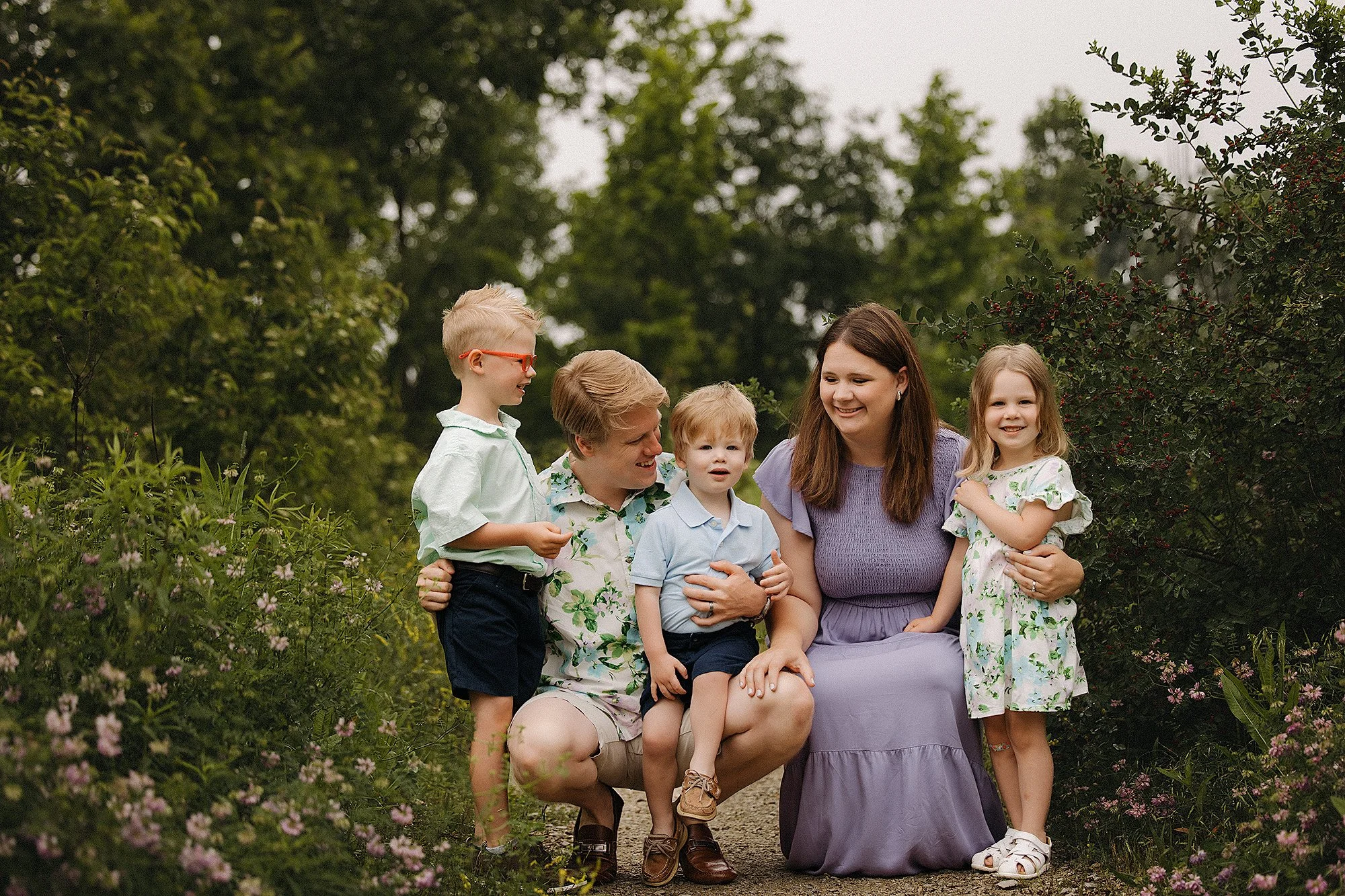 "Family of five wearing soft pastel and coordinated outfits during an outdoor garden portrait, offering beautiful inspiration for what to wear for family photos with timeless colors and natural style