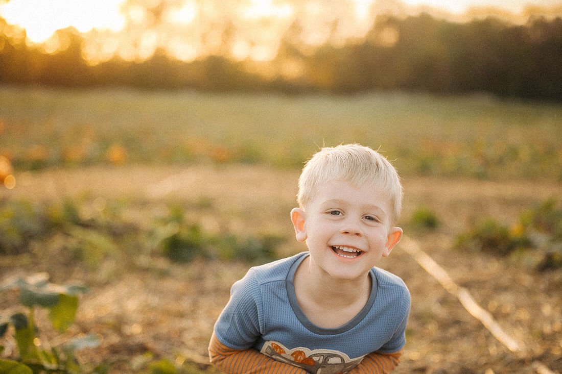 Smiling young boy poses in the warm evening light of a pumpkin field during his family’s visit to Dull’s Pumpkin Harvest