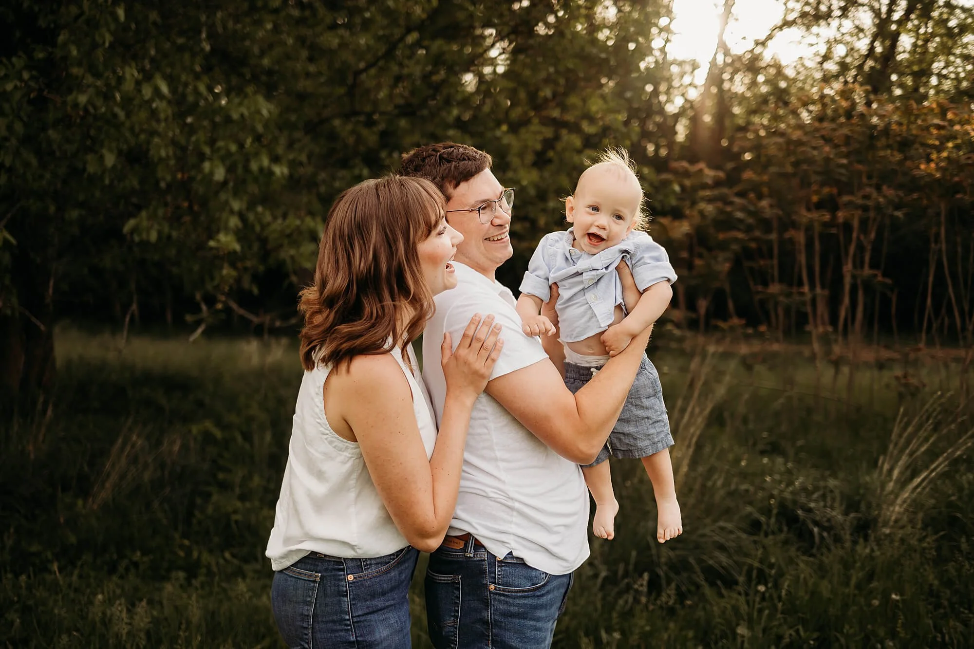 A family enjoys a spring photo session in the park, dressed in light, colorful clothing surrounded by lush greenery.
