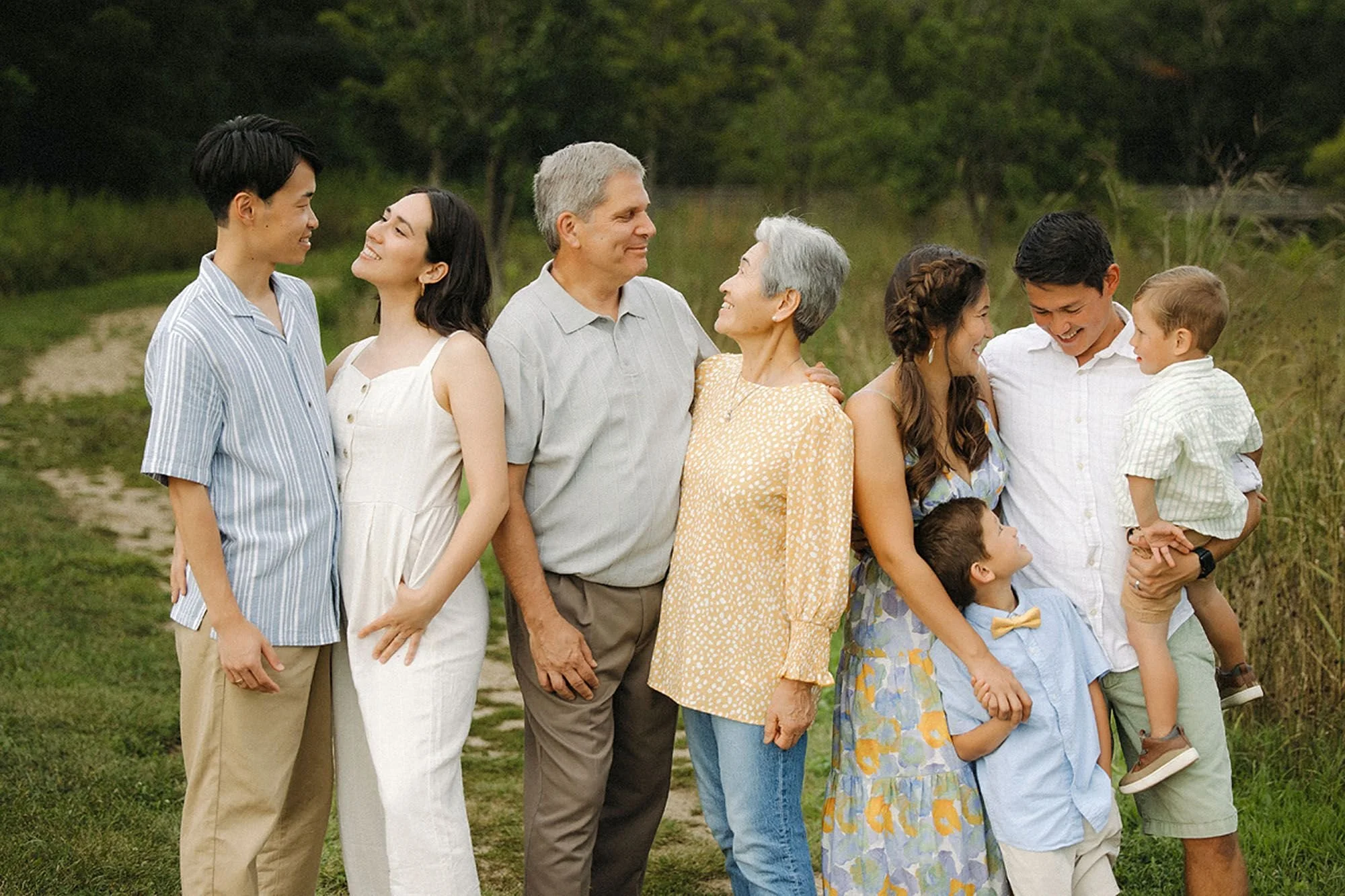 Three generations of an extended family laughing together in a field during their Flat Fork Creek Park photo session
