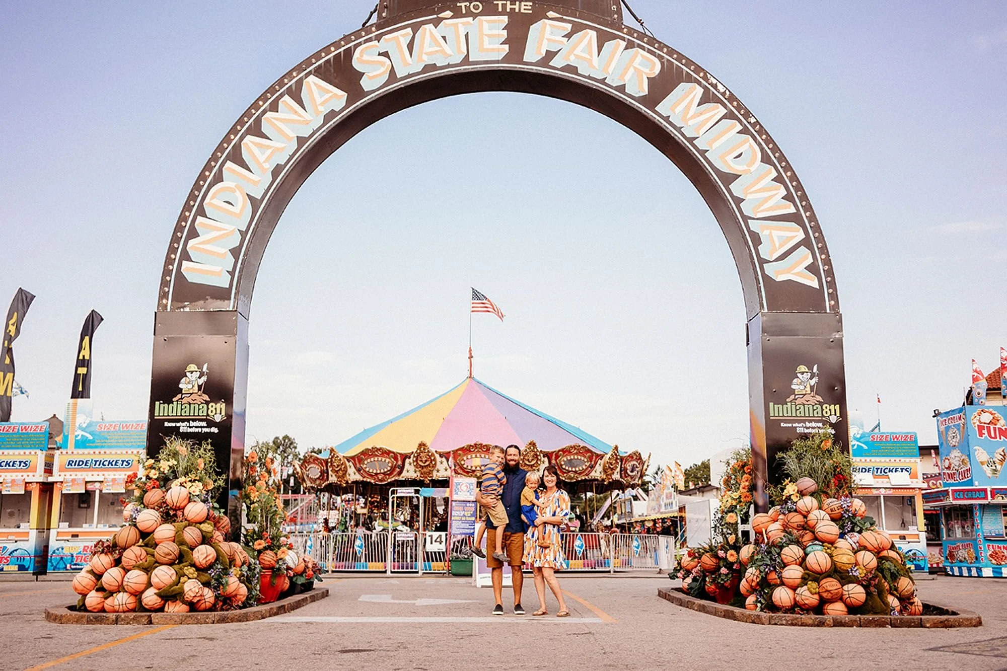 Joyful family poses together at an Indiana State Fair, surrounded by colorful carnival lights in the background.