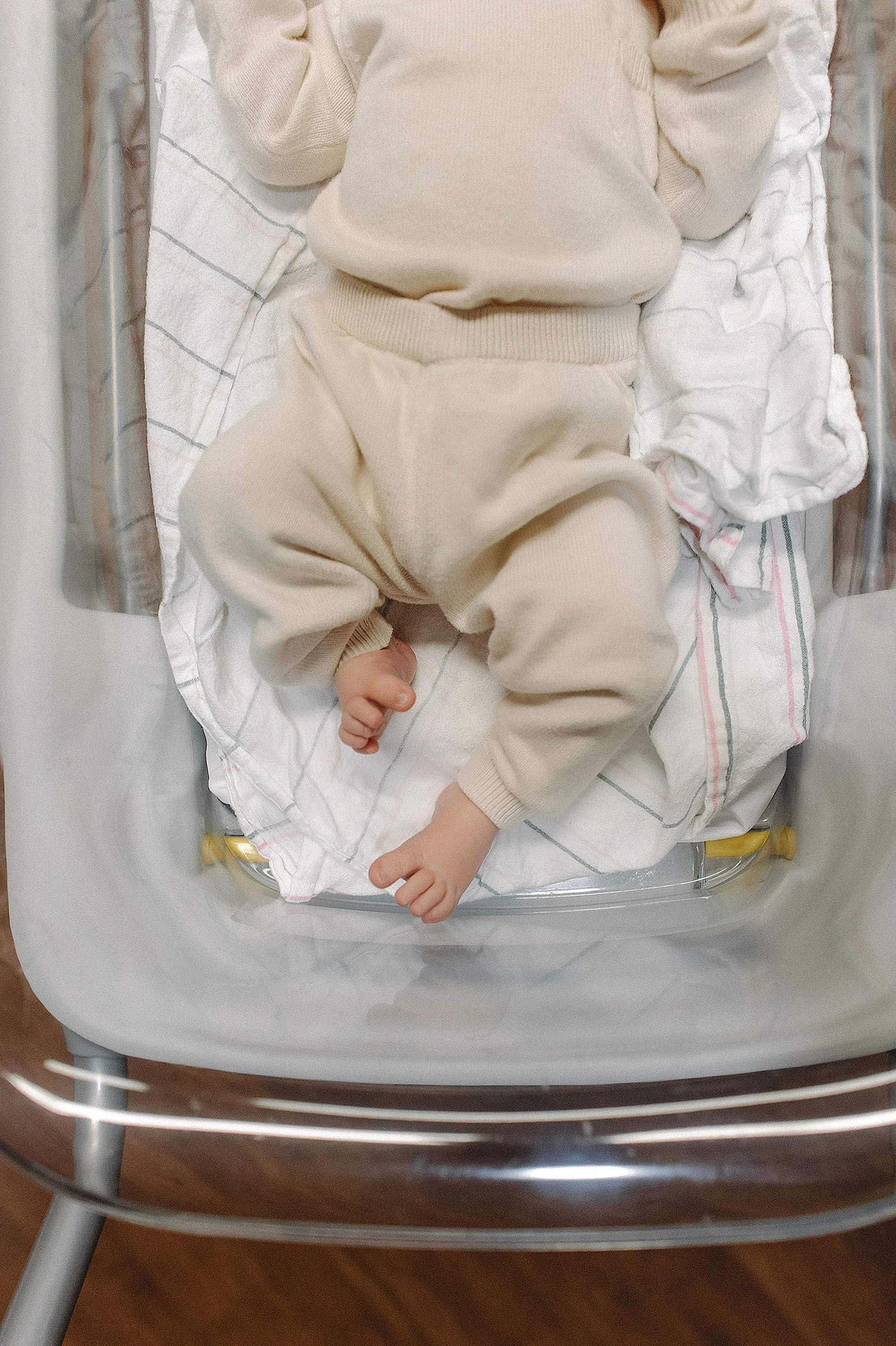 A baby in beige clothing lying in a hospital bassinet with a white and blue striped blanket.