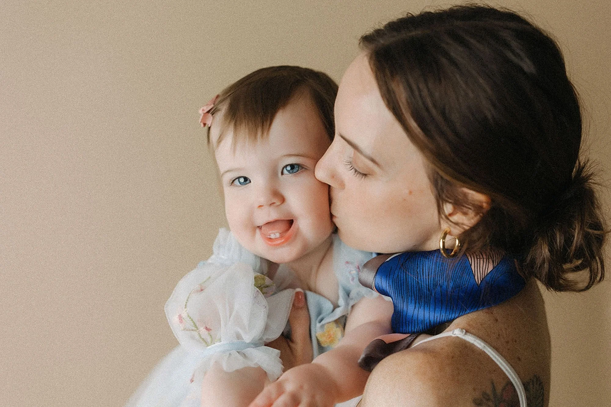 Mother kissing her laughing baby girl's cheek, candid portrait captured during a simple cake smash photography session