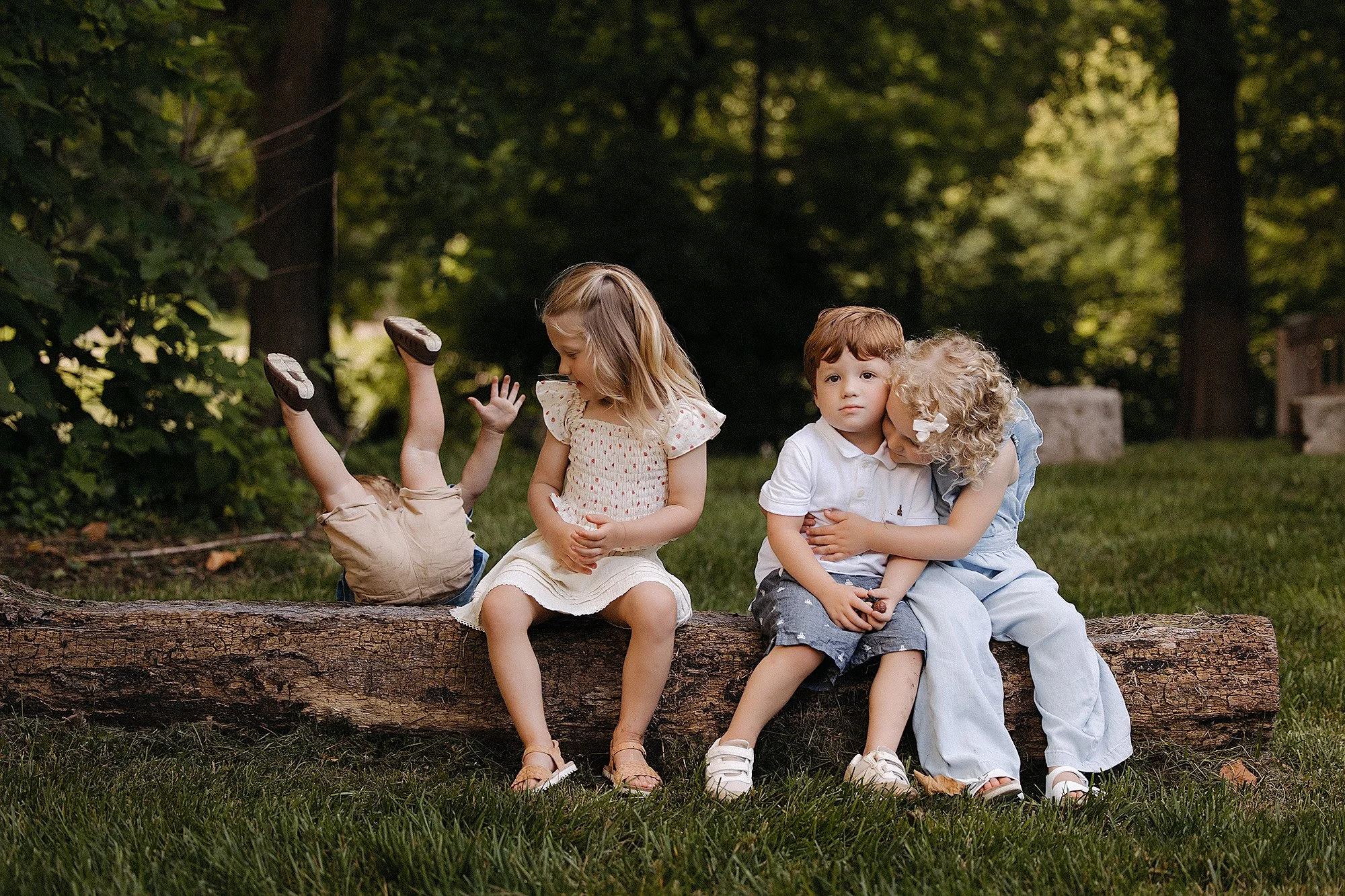 Four children sitting on a log, one upside down playfully with legs in the air during family session in Indiana.