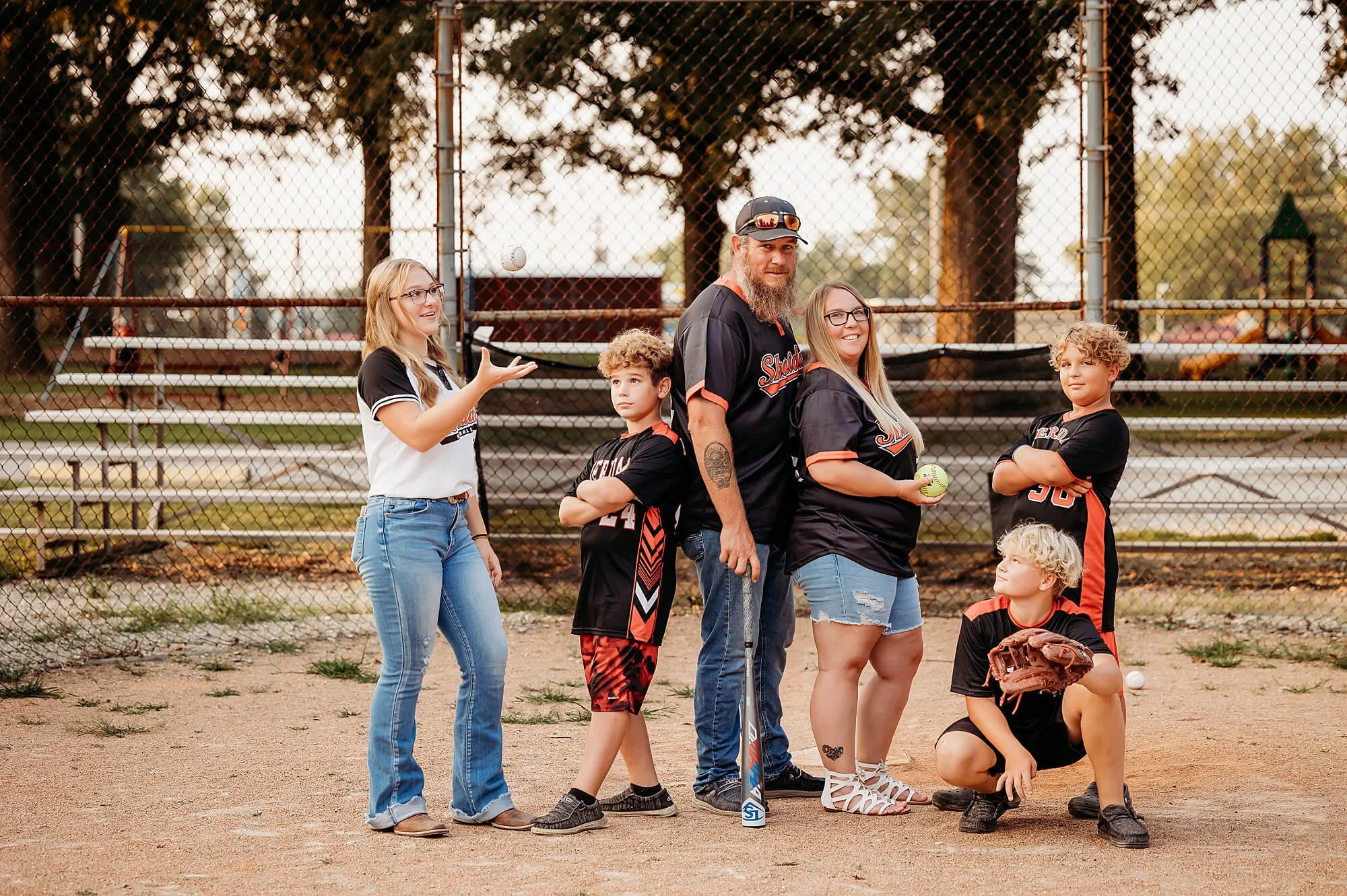 A joyful family photo on a baseball field, featuring older kids celebrating a pregnancy announcement together, captured by theheartnarrative Indiana Photographer