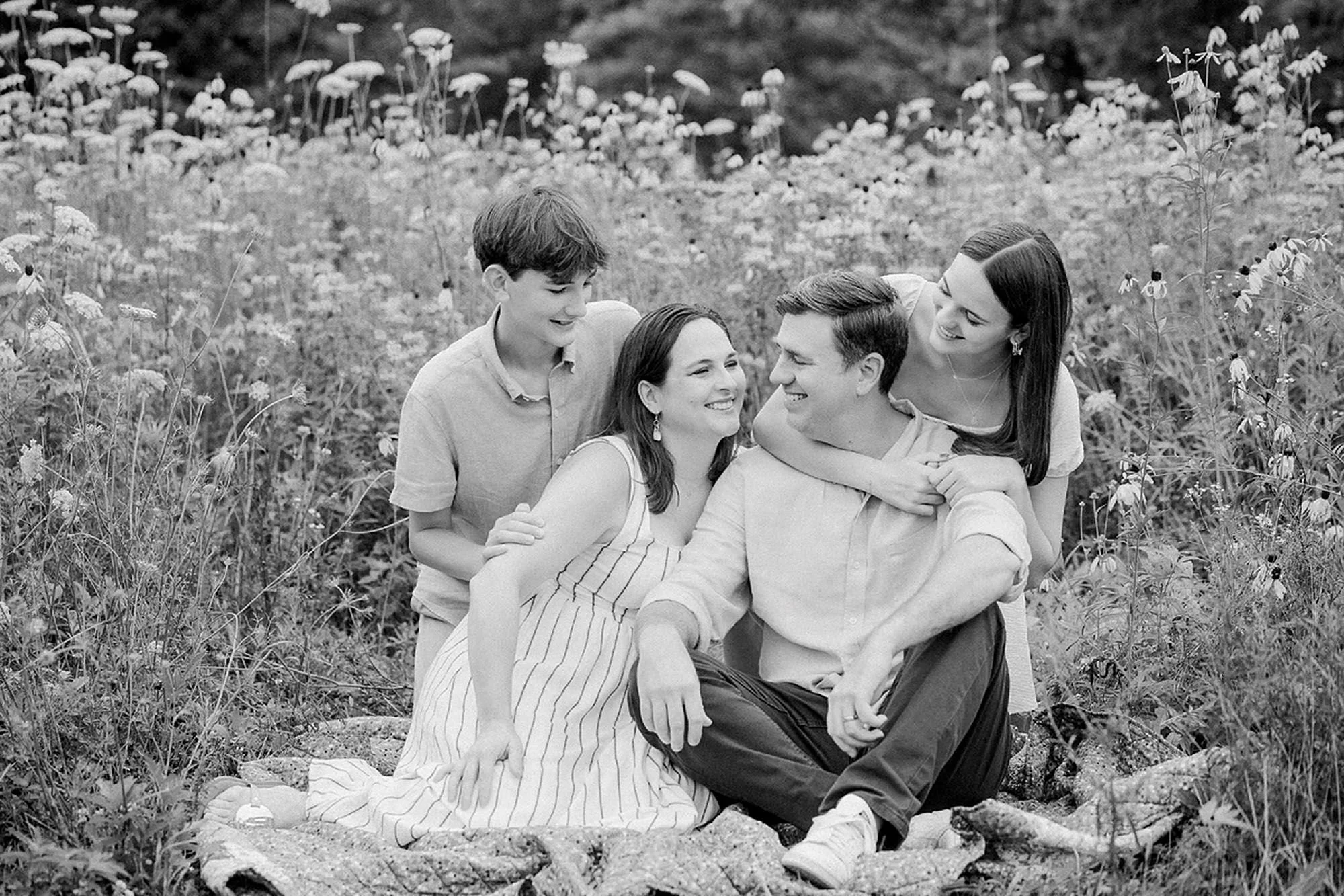 A family of four sitting together on a blanket in a wildflower field during a summer session.