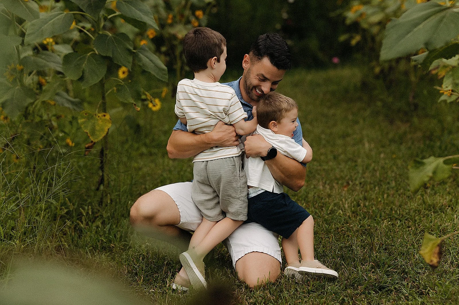 Lifestyle family photography Indianapolis with dad hugging two young boys in sunflower field