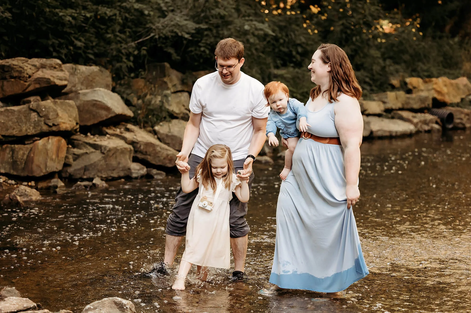 A family stands together in the water, their daughter in front, all wearing spring clothing for a photo shoot