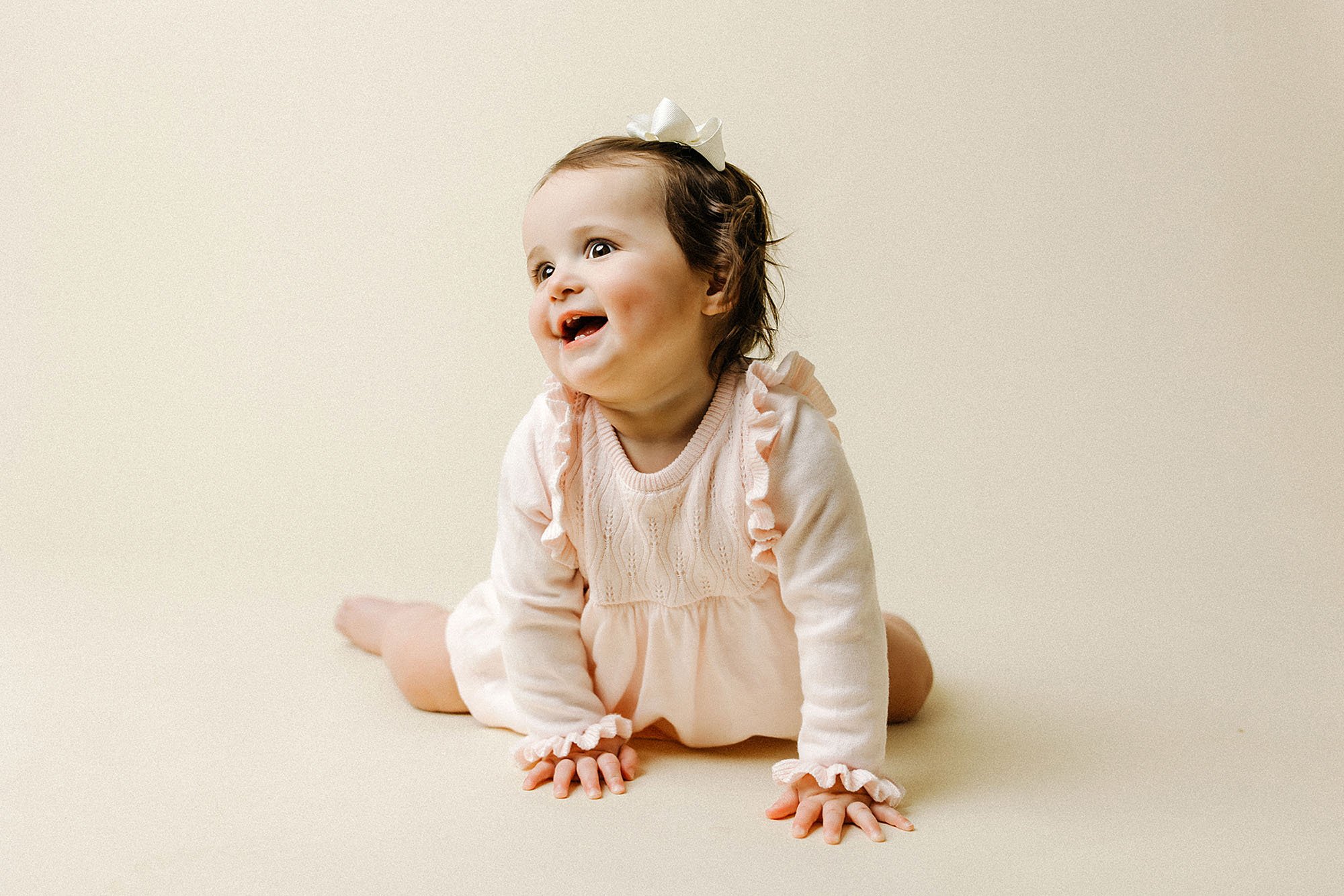 A baby girl in a pink dress sits on the floor, celebrating her first birthday during a photography session in Westfield, Indiana