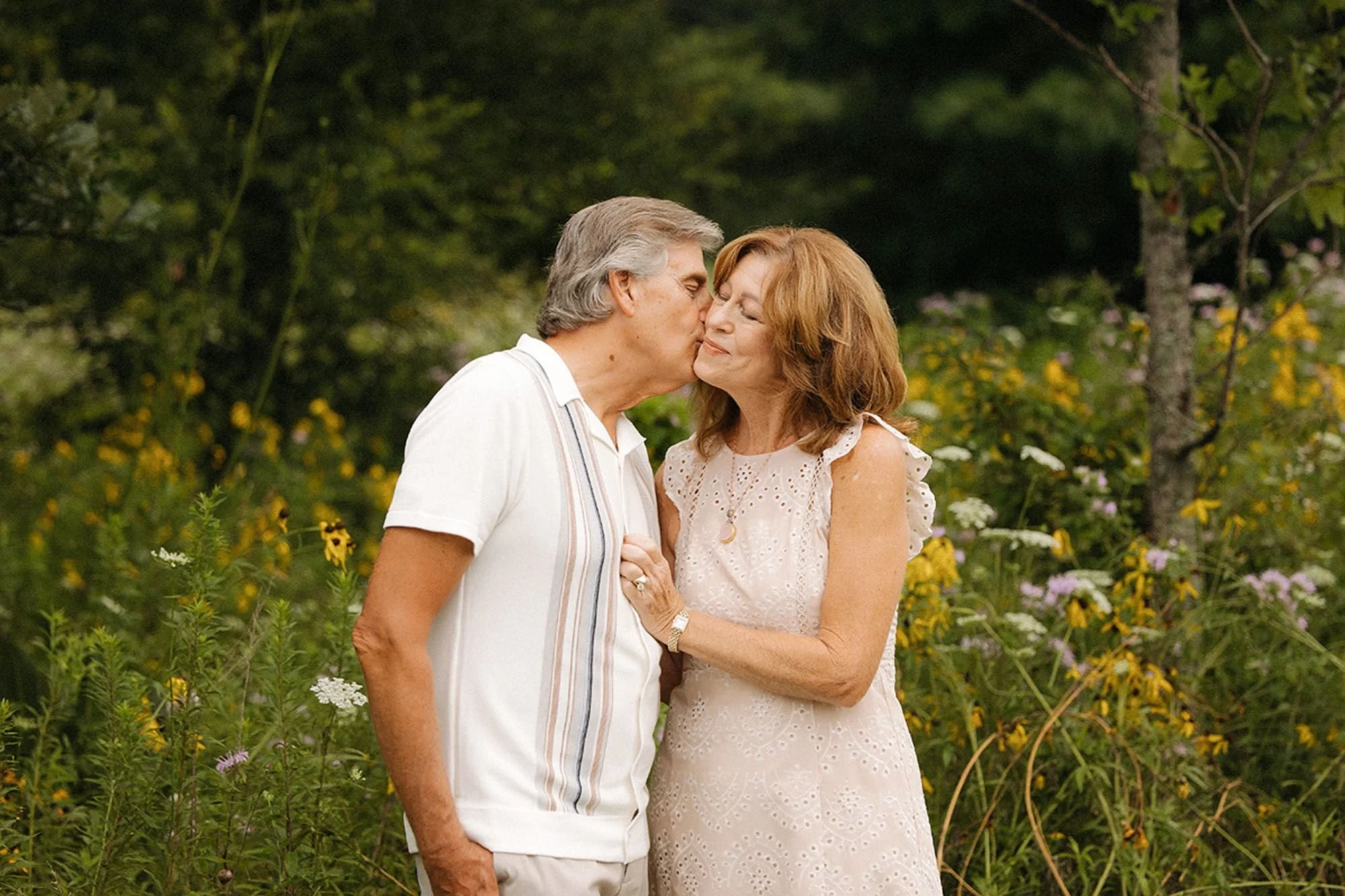 Grandparents sharing a kiss surrounded by wildflowers during an extended family session in Westfield, Indiana.