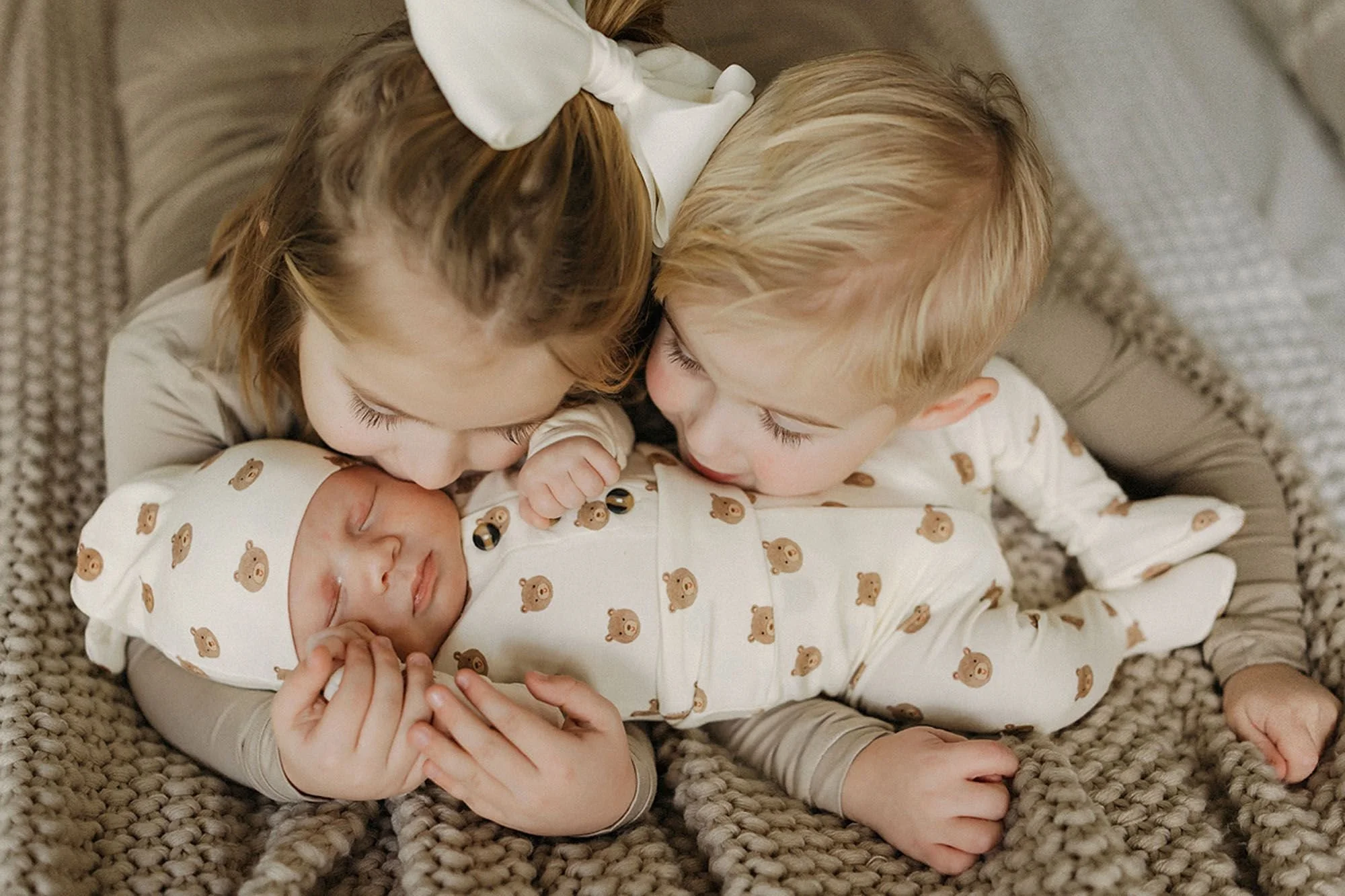 Heartwarming newborn photography with loving siblings gently cuddling and kissing their sleeping baby brother