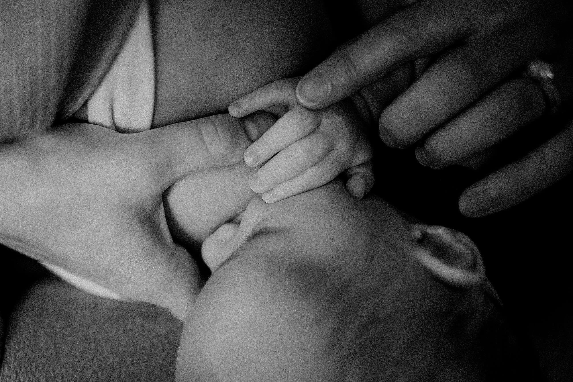 A close-up, black-and-white photo of a woman lying down with her hand on her lap, a small child's hand gently touching her chest, and the child's face slightly visible as they look up.