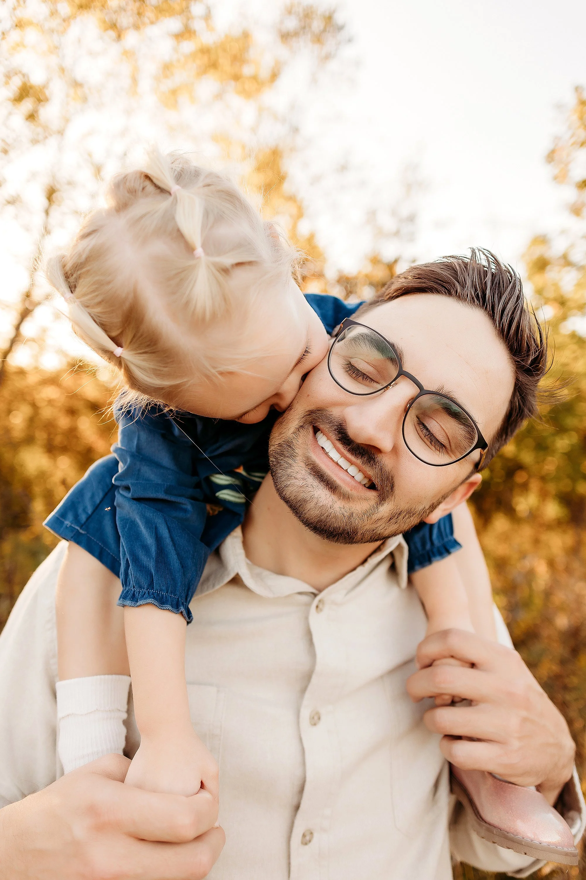 A man with glasses and a young girl enjoying a sunny day together in a park during a Mini Session photo shoot.