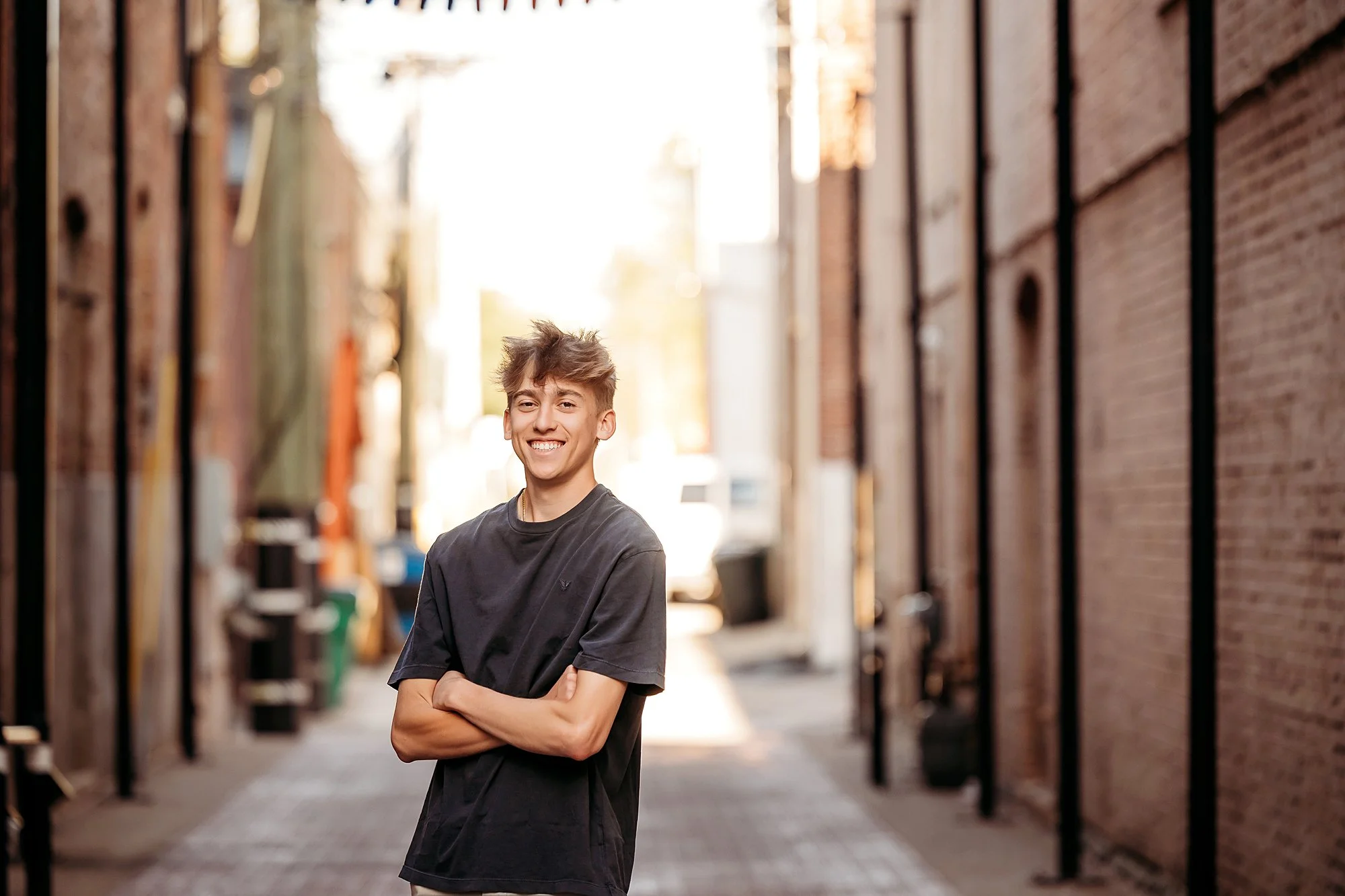 Young man stands confidently in an alleyway, captured during his senior photo session in downtown Noblesville during