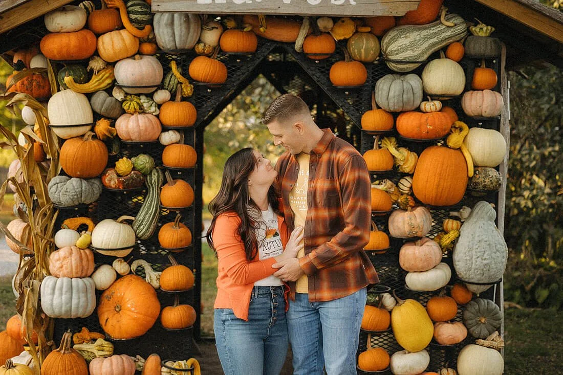 Couple standing together beneath a colorful arch of pumpkins and gourds during their autumn family visit to Dull’s Pumpkin Harvest