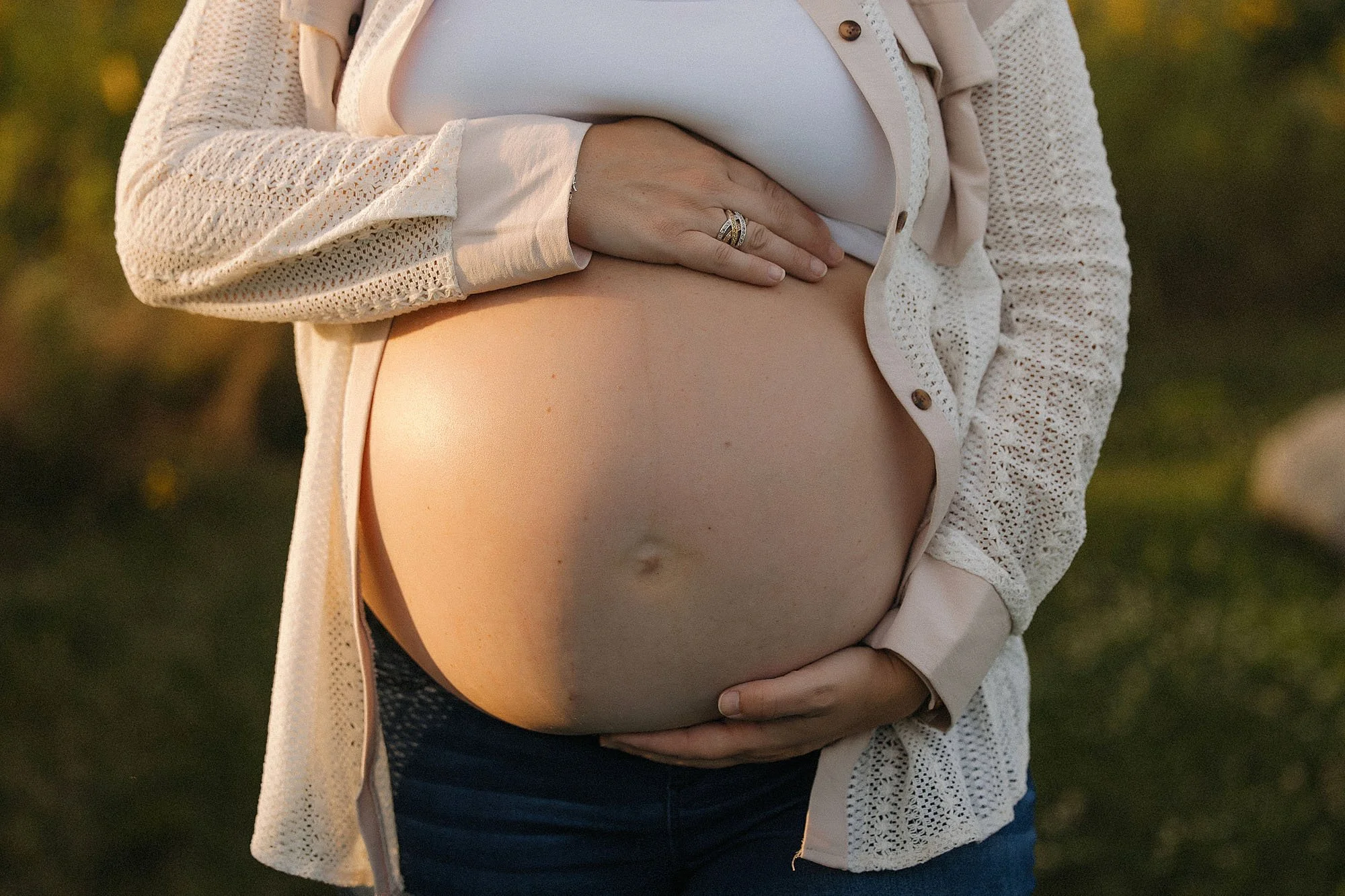 Close up maternity photo of pregnant belly with hands resting gently during golden hour in Indiana