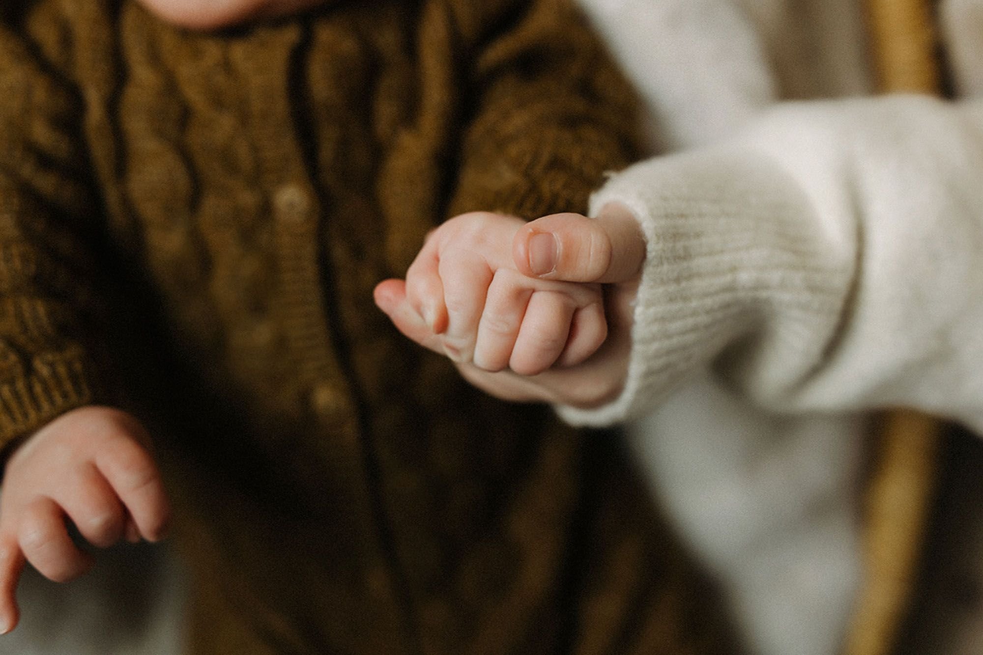 Close-up of a newborn baby's tiny hand gently holding an older sibling’s finger, and timeless lifestyle newborn photography with meaningful sibling bonding moments