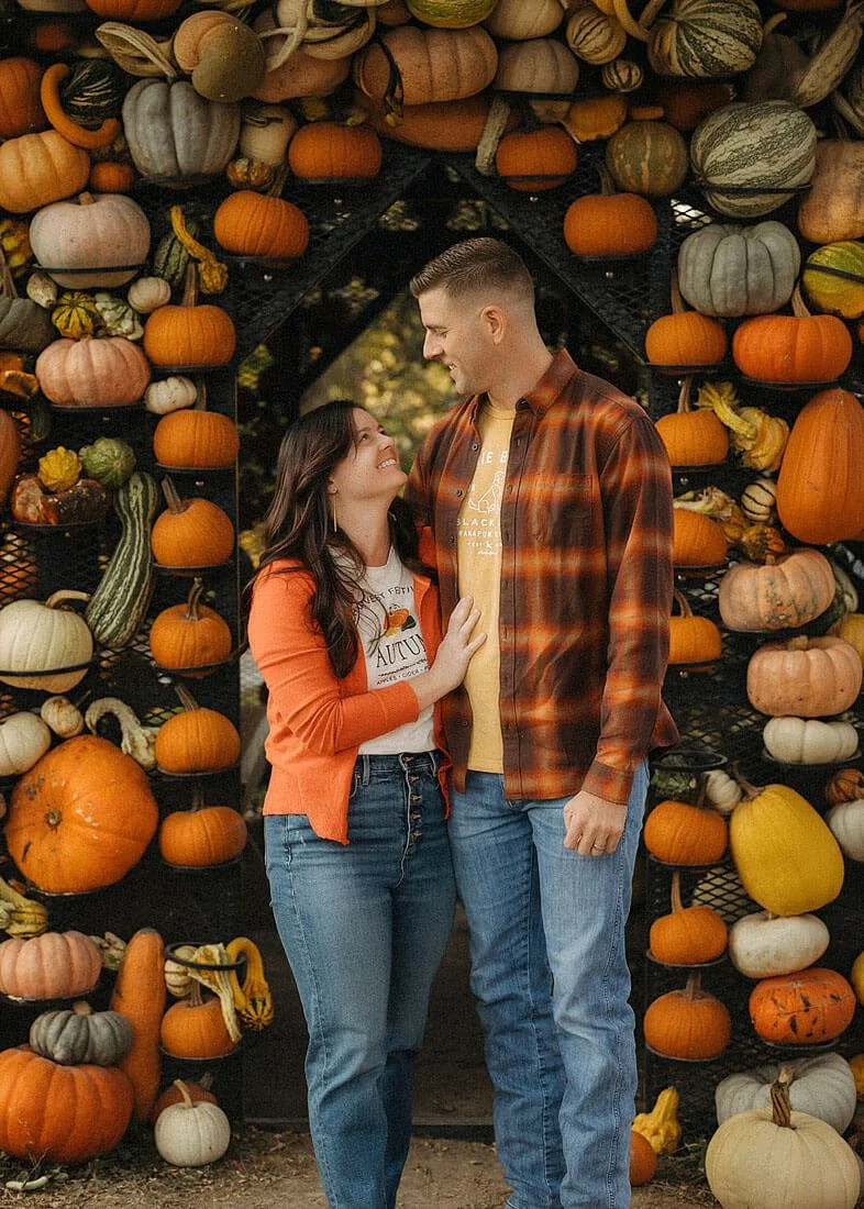 Couple sharing a sweet moment beneath a colorful pumpkin display during their fall family photography session at Dull’s Pumpkin Harvest