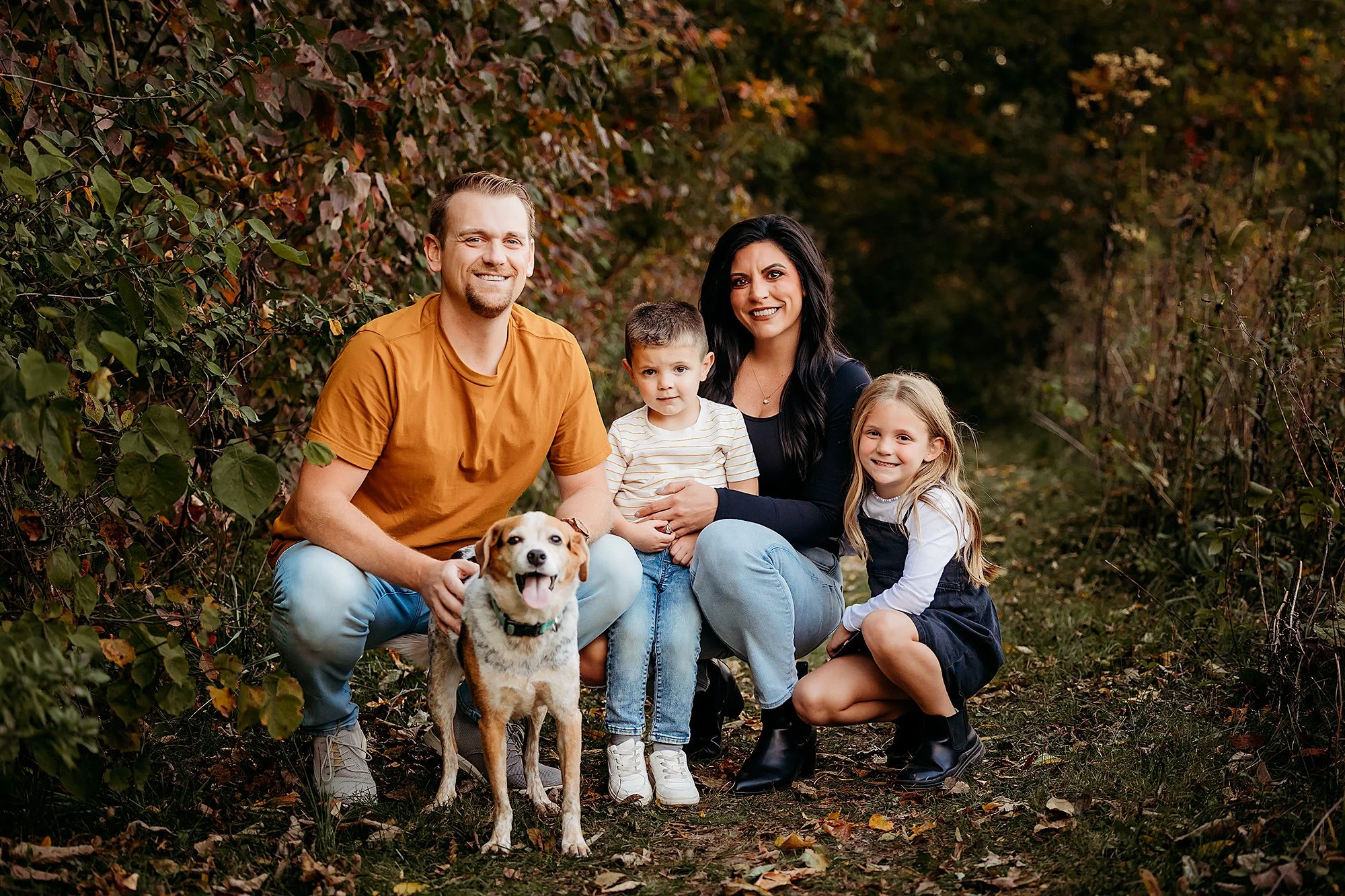 Happy family with their dog wearing coordinated neutral fall outfits during an outdoor autumn portrait session, showcasing what to wear for family photos with timeless, stylish, and color-coordinated clothing