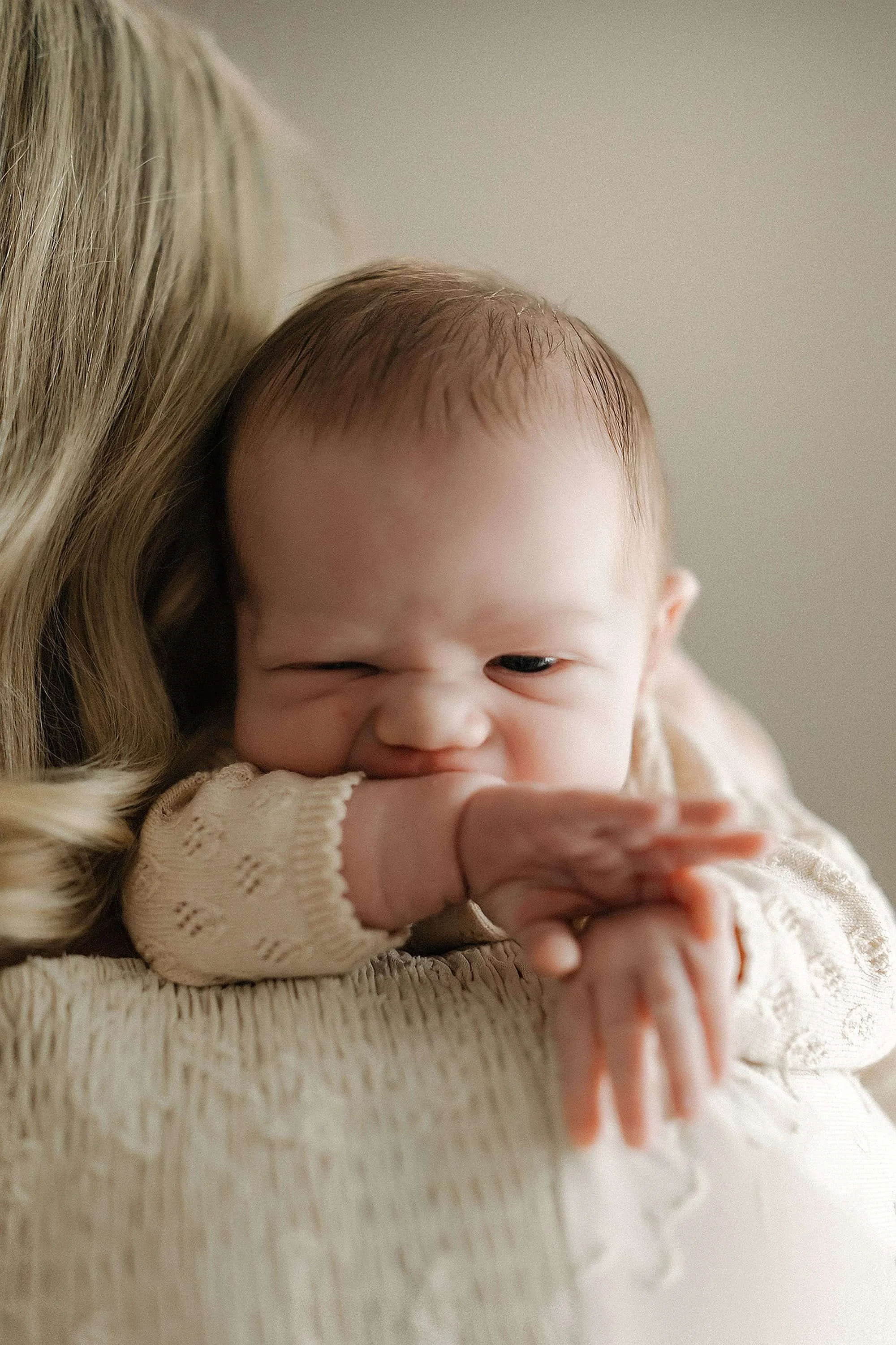 Close-up of a baby girl resting her chin on her arm, lying on an adult's shoulder, with a gentle expression and a cozy beige sweater.